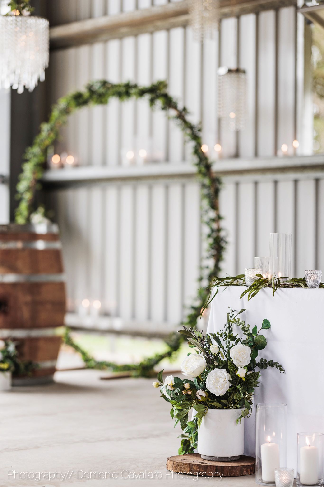 White floral arrangements with greenery and candles decorate a rustic wedding venue entrance.