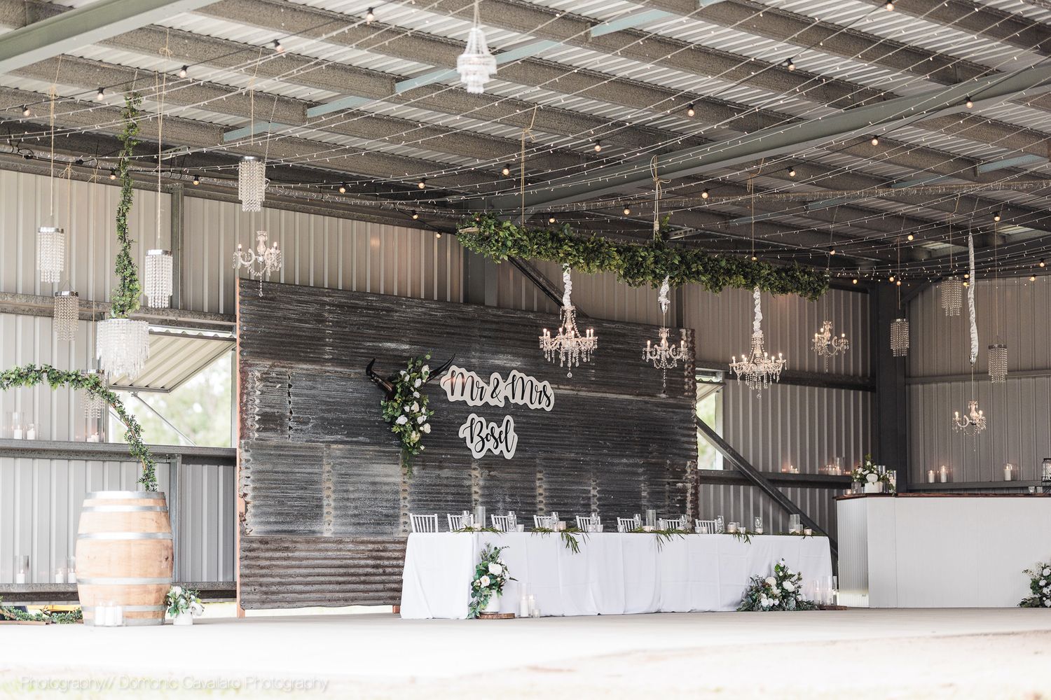 Modern rustic wedding venue interior with wooden accent wall, white buffet table, and hanging crystal chandeliers.