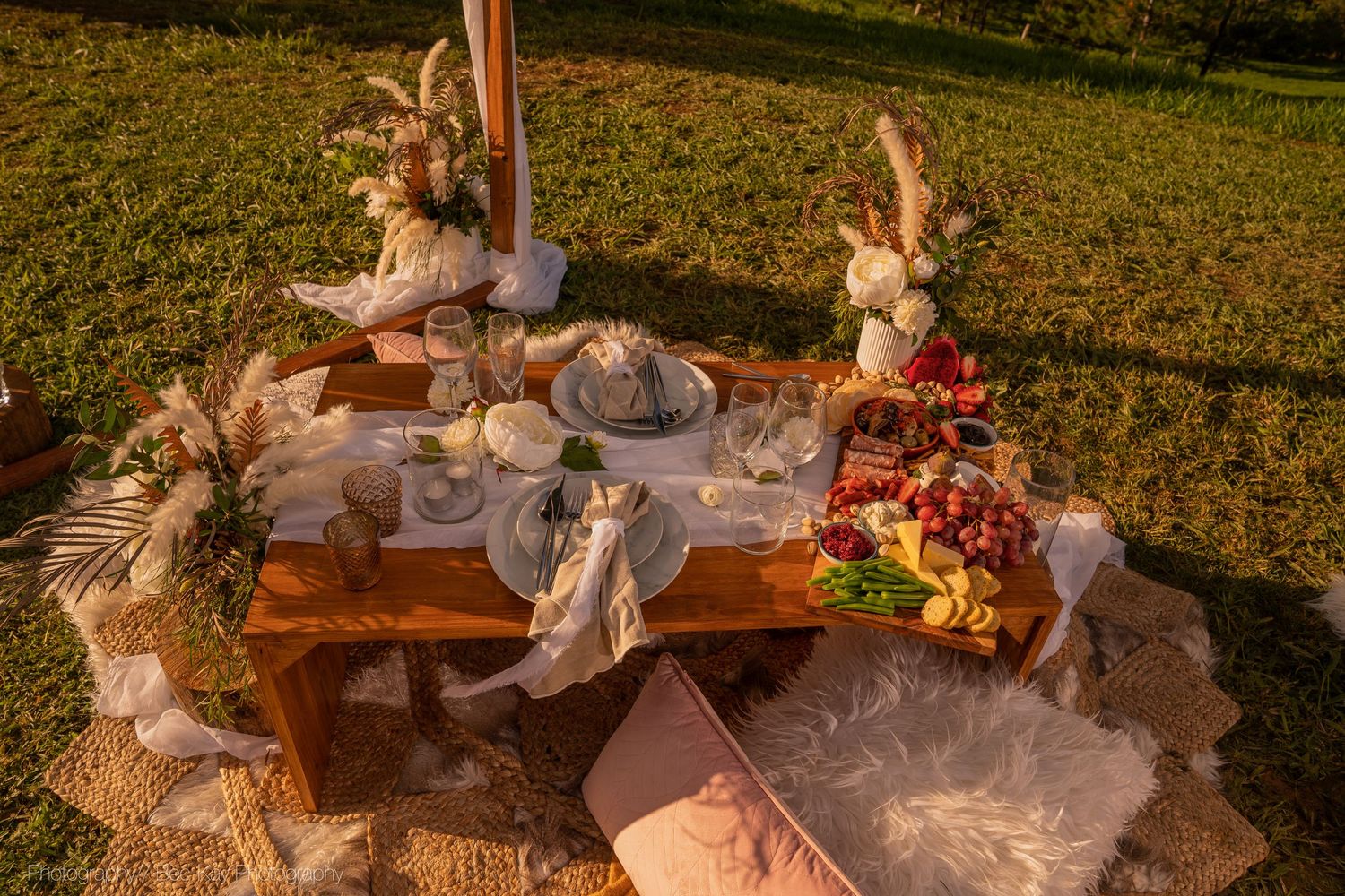 Rustic outdoor picnic setup with plush cushions, decorative bunnies, and glowing string lights at golden hour.