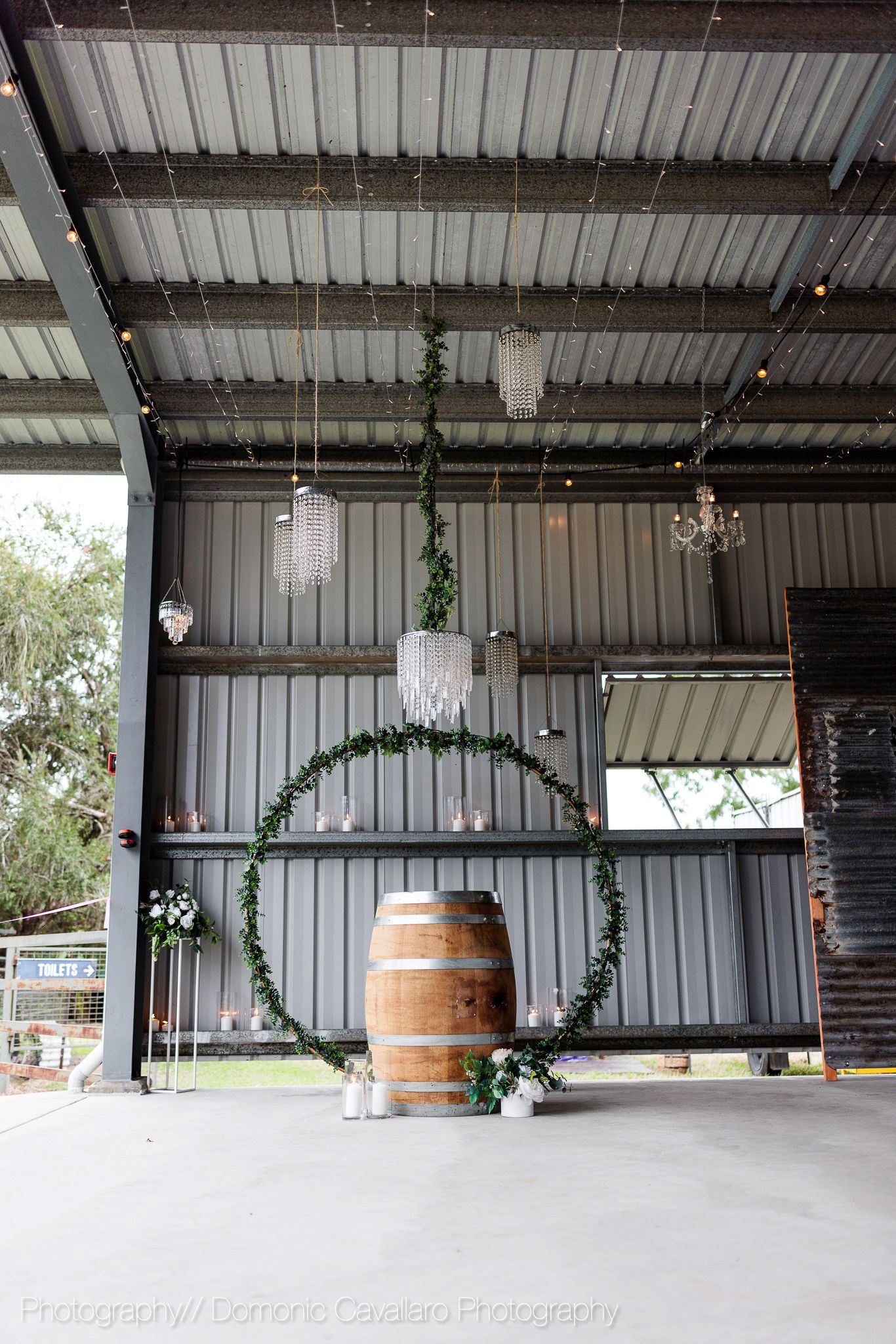 Industrial barn venue decorated with greenery hoop arch and wooden barrel for wedding ceremony.
