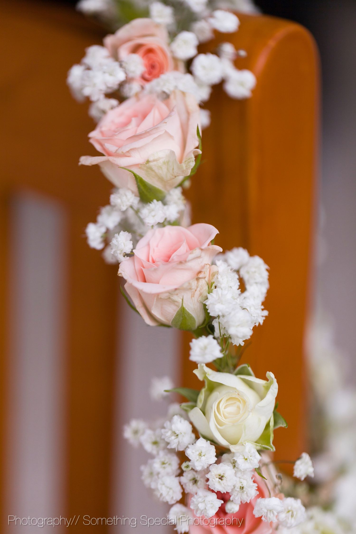 Delicate pink and white roses arranged with baby's breath flowers against an orange background in soft focus.