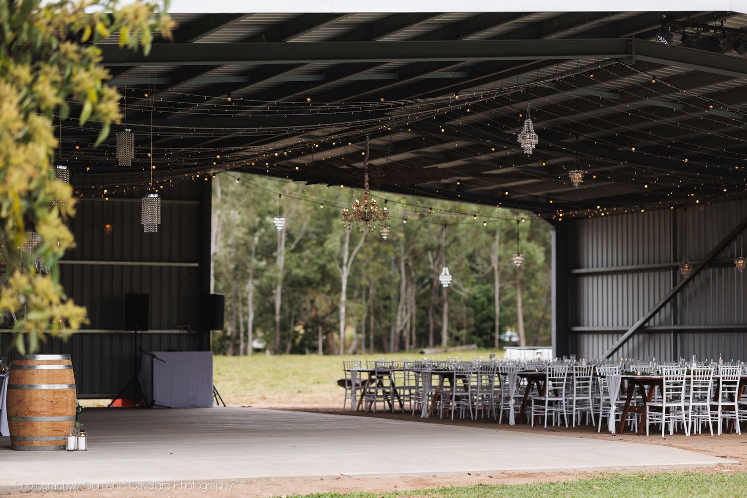 Open-air barn wedding venue with rustic wooden barrels and views of trees through large doorway opening.