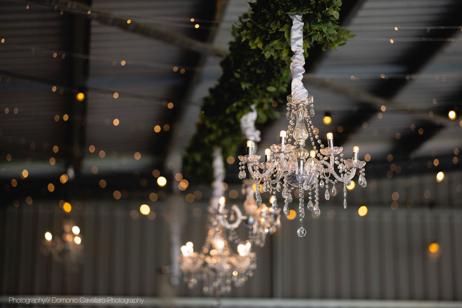 Crystal chandeliers and string lights create a romantic ambiance against an industrial ceiling backdrop.