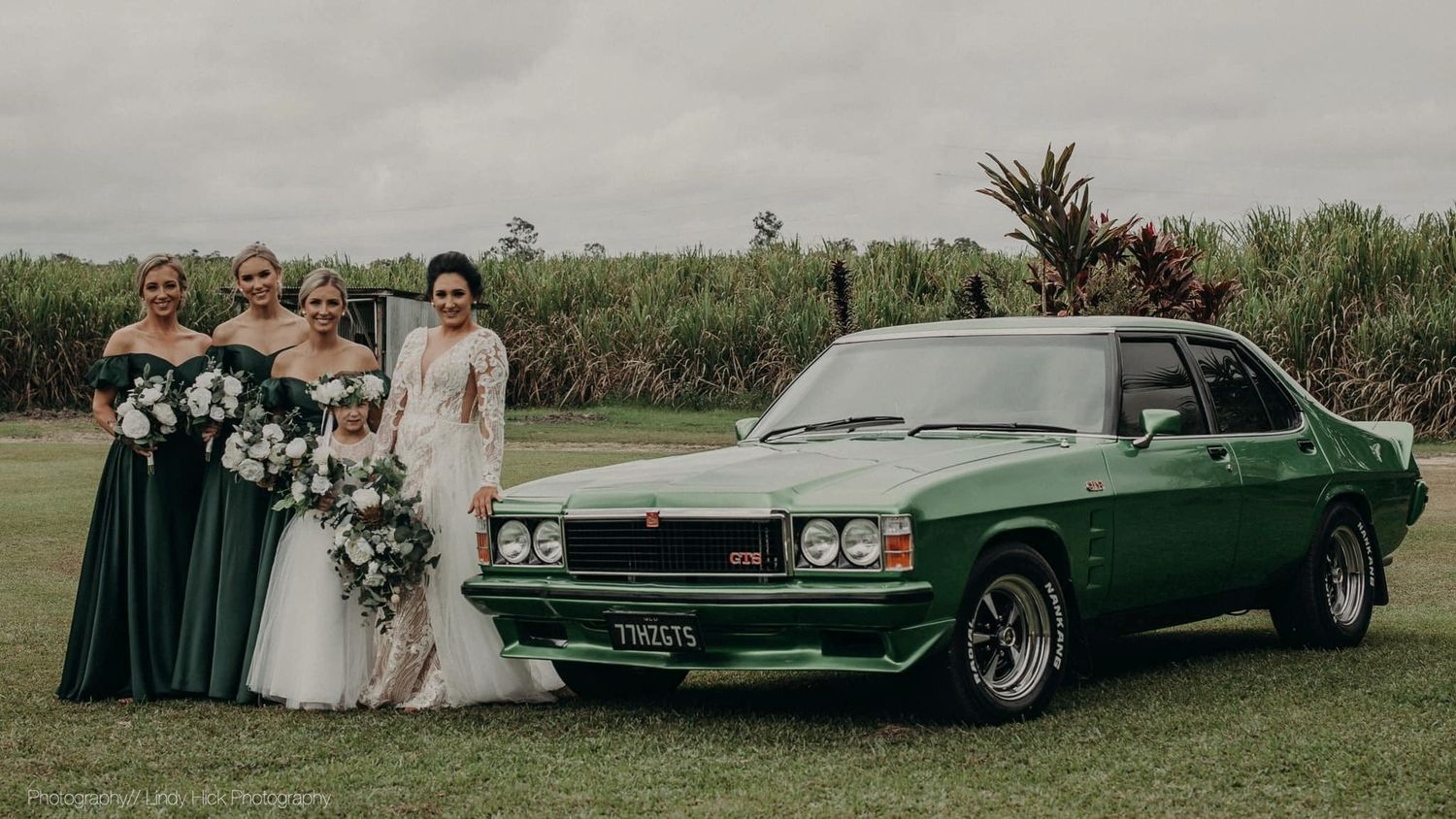 Classic green Holden muscle car parked on grass with wedding party.