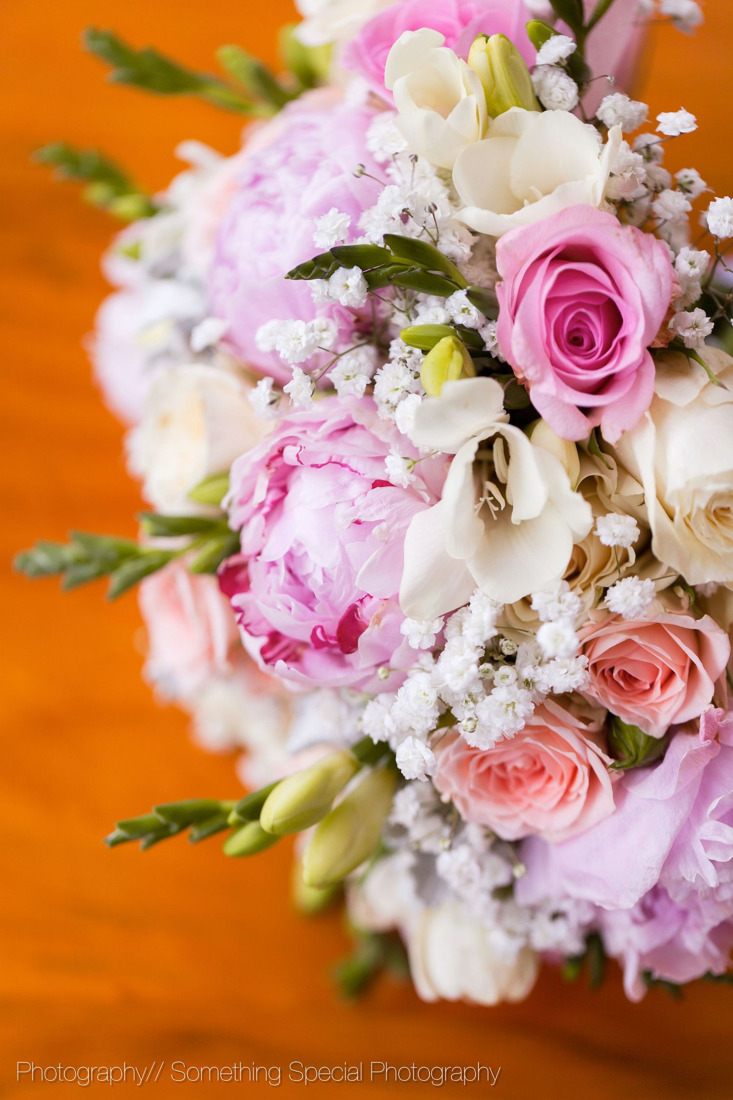 Close-up of an elegant bridal bouquet with pink peonies, roses, and white flowers against an orange background.