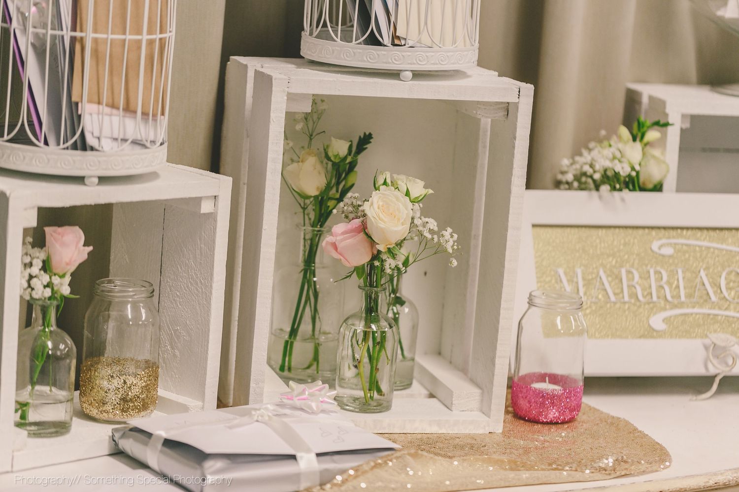 White decorative frames with delicate pink roses in glass vases on display at a wedding styling setting.