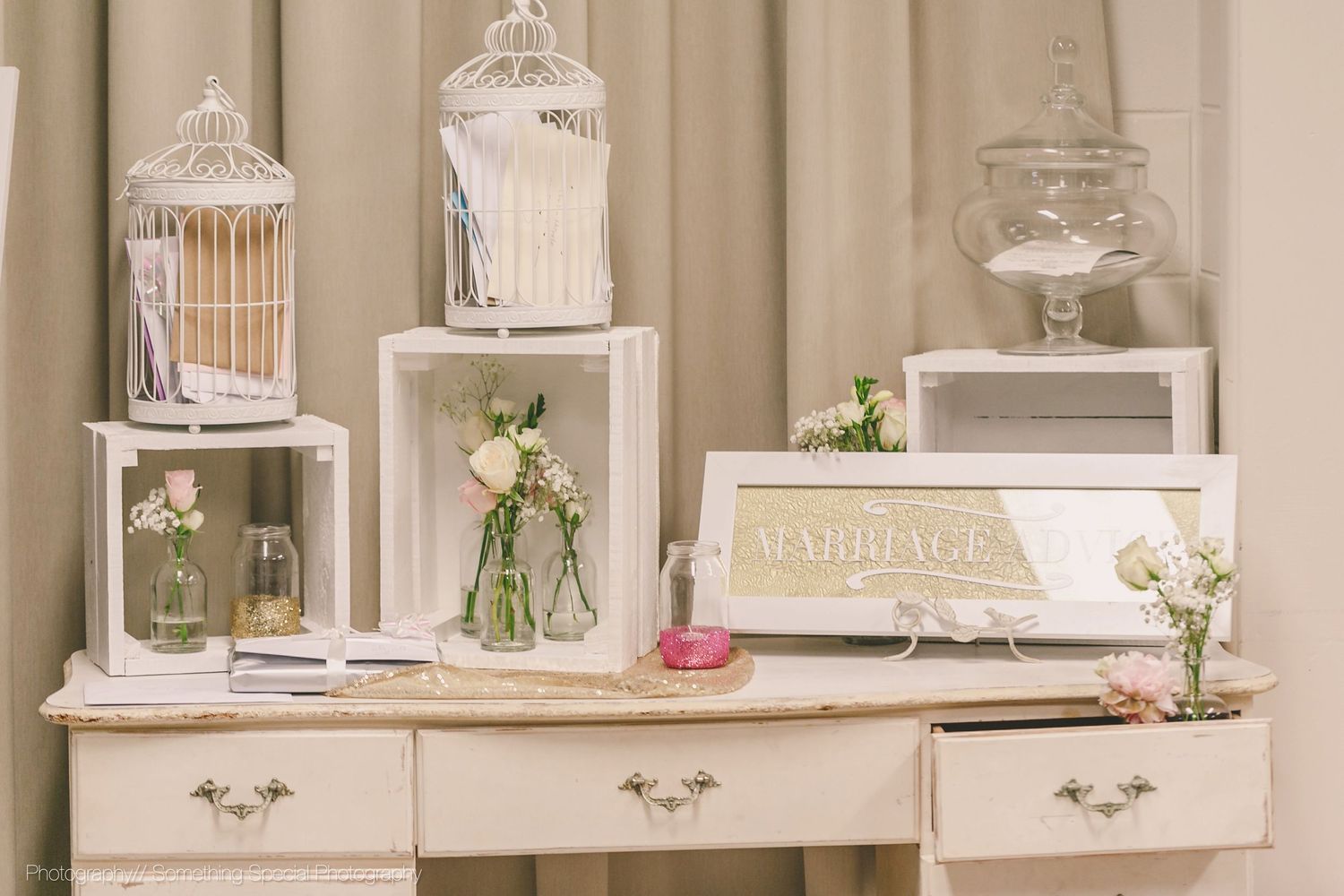 Elegant white vanity table decorated with vintage lanterns, glass jars with flowers, and ornate accessories.