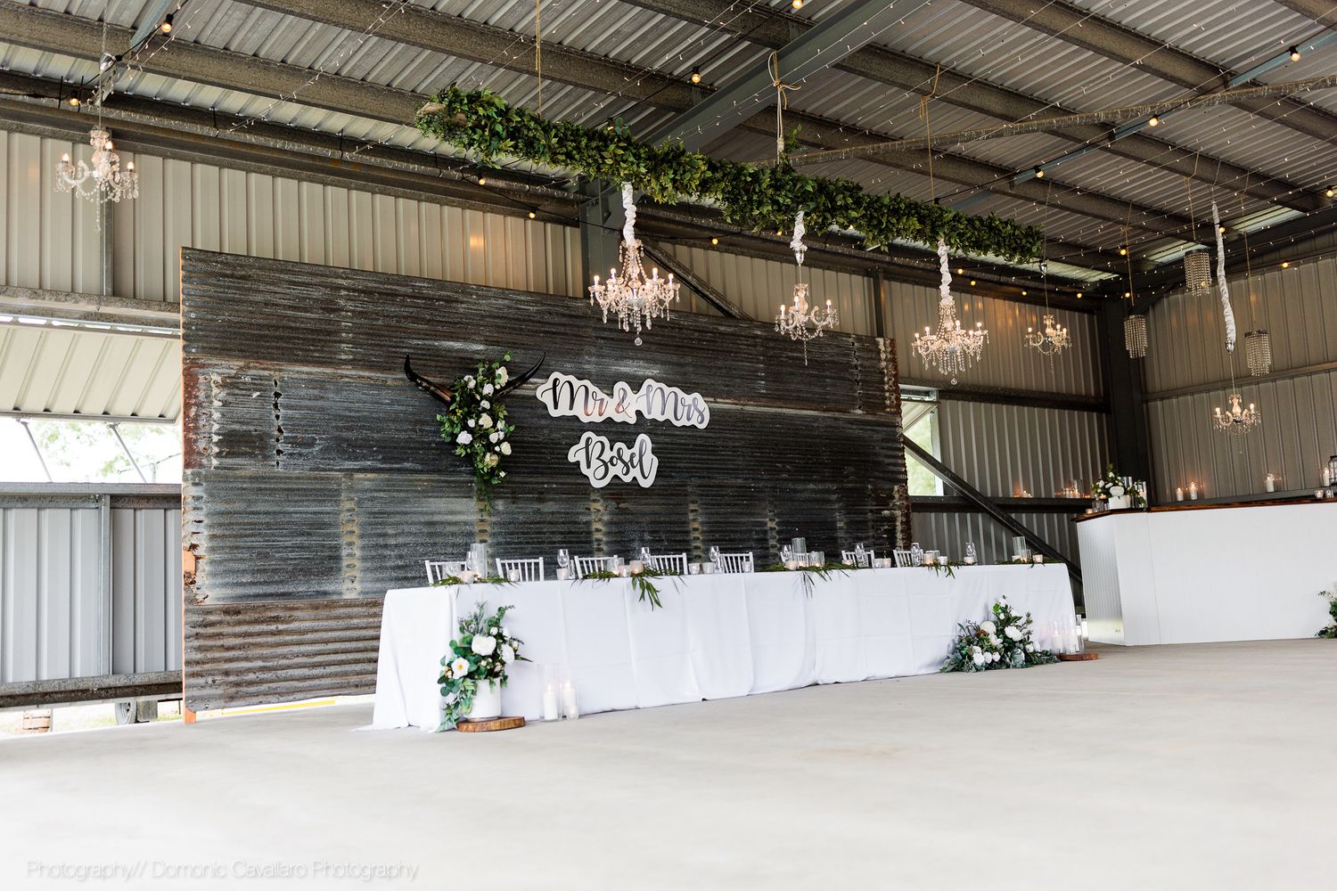 Modern barn wedding reception space with white tables and rustic wooden wall decor.