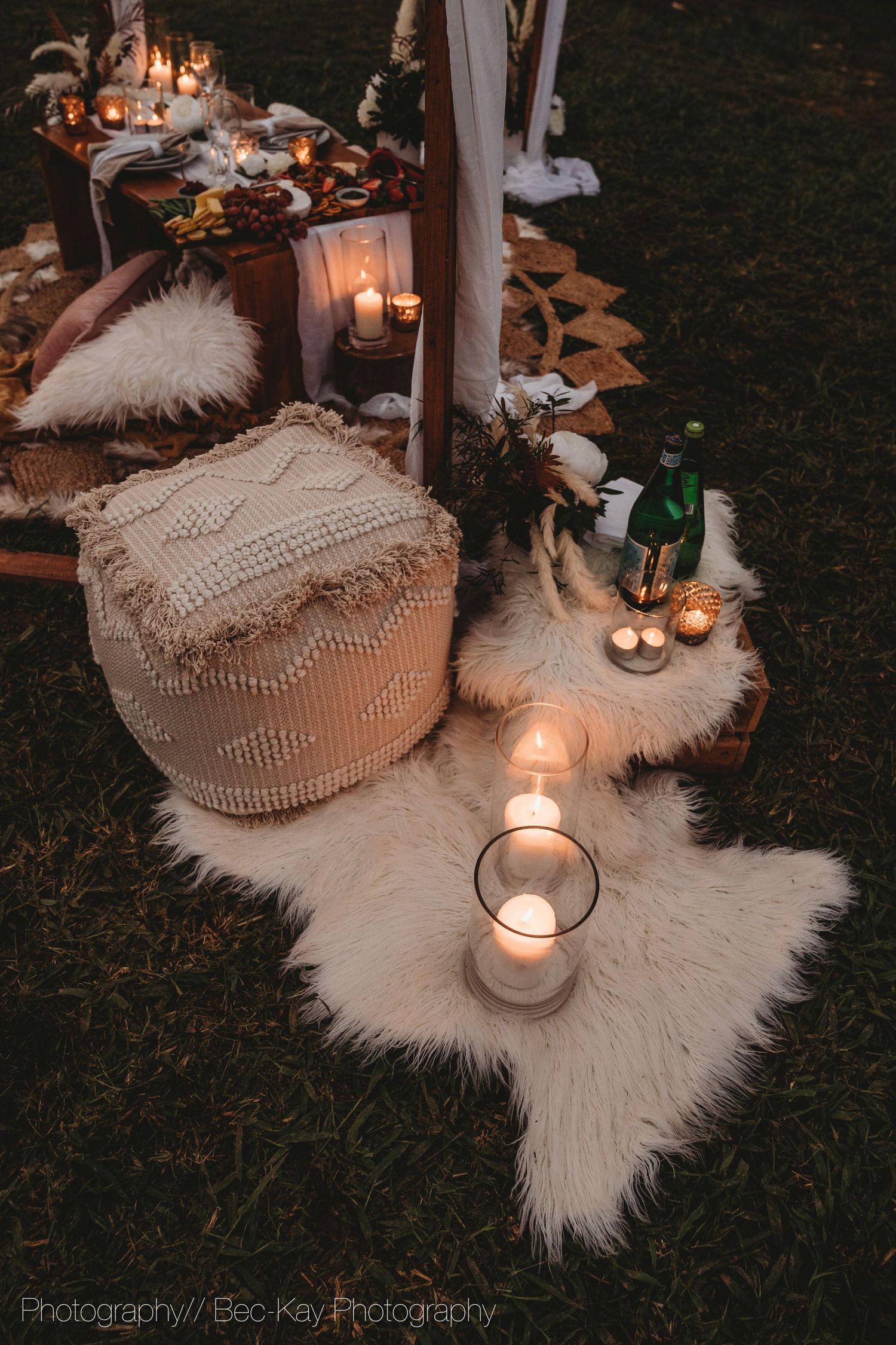 Cozy bohemian outdoor setting with candles, fur rugs, and macrame decor creating a warm ambiance at dusk.