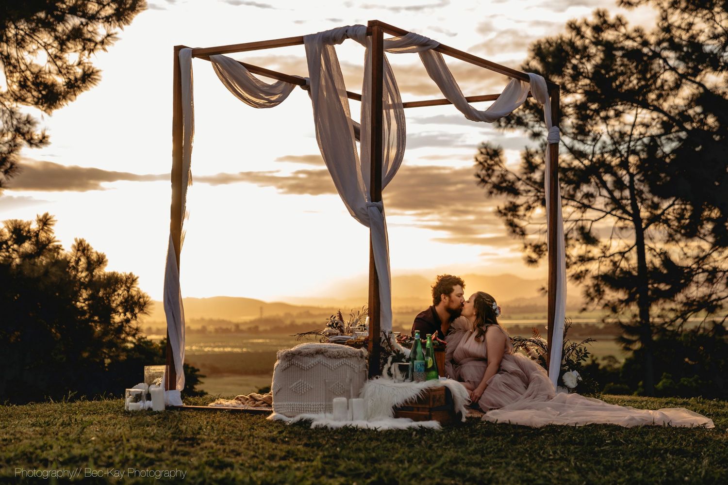 A romantic sunset picnic setup with a draped canopy frame and blankets on the grass during golden hour.