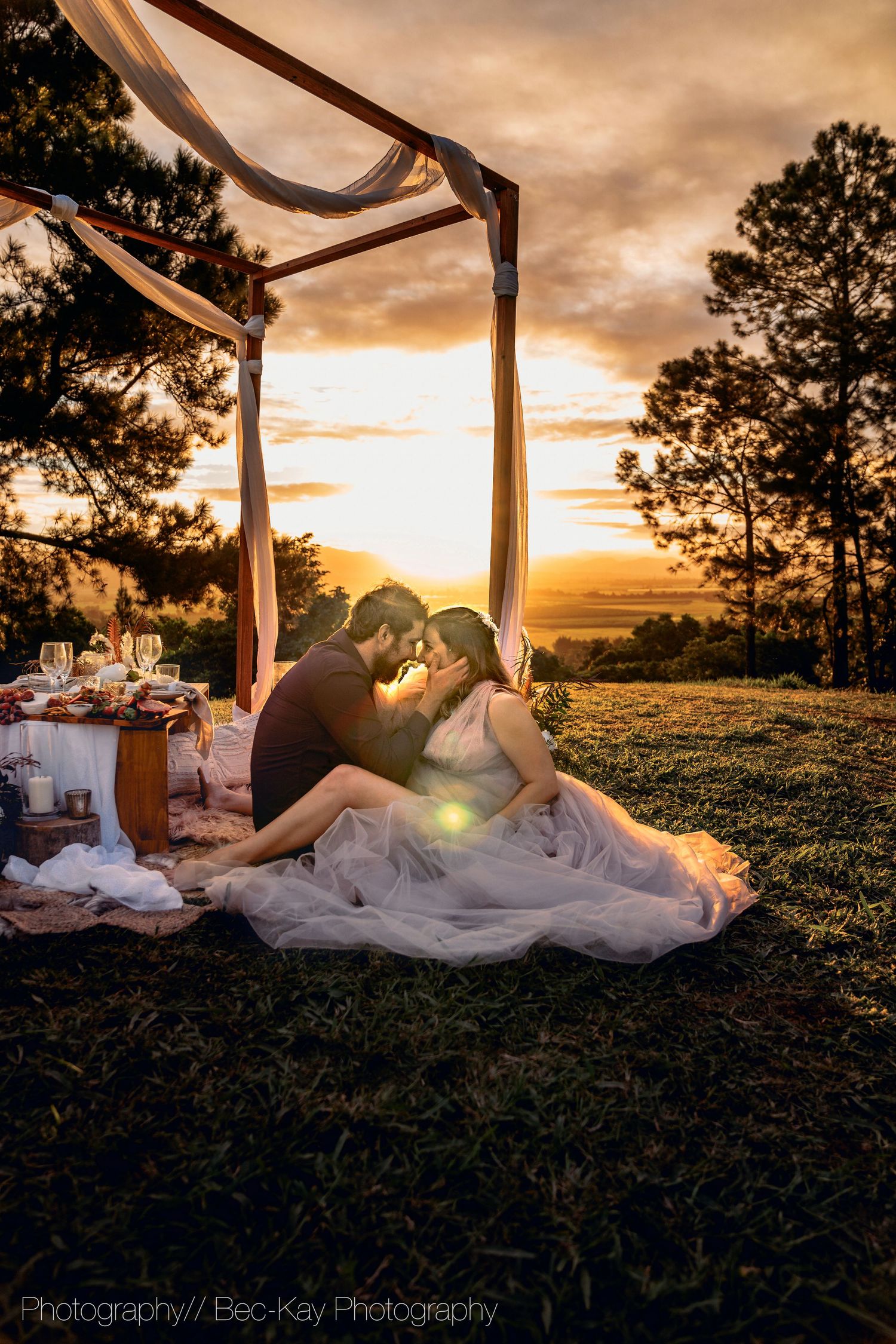 Romantic sunset picnic scene under draped fabric canopy with couple silhouetted against dramatic orange sky.