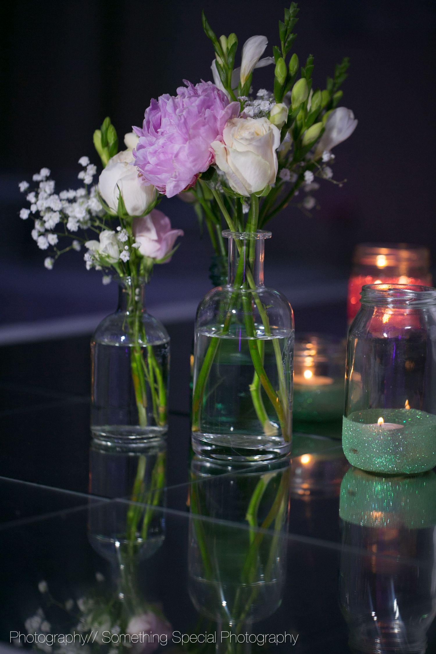 Glass vases with pink and white flowers and baby's breath next to glowing candles in mason jars.