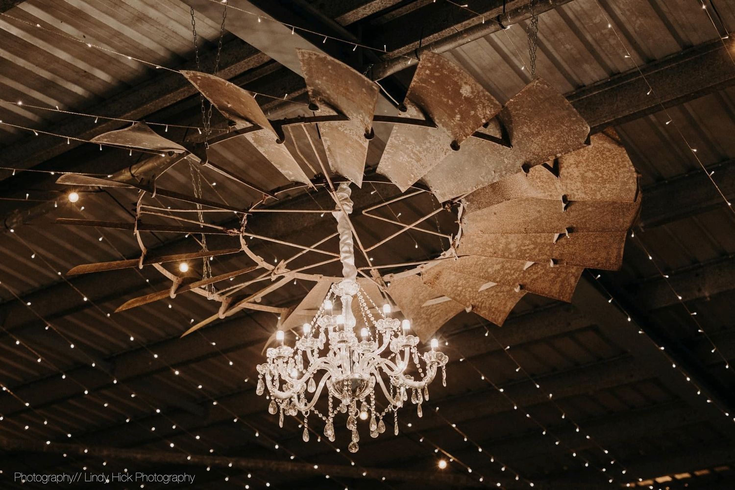 A grand crystal chandelier suspended beneath a wagon wheel ceiling fixture with twinkling fairy lights above.