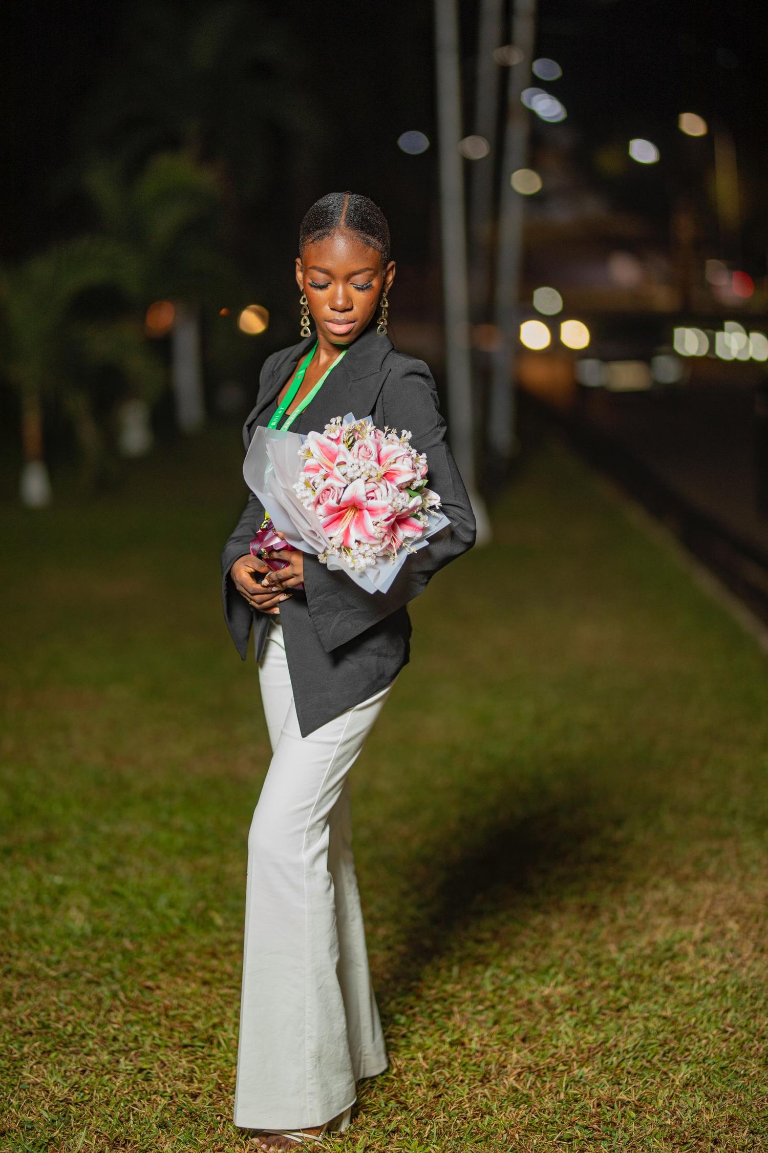 Graduate in formal attire holds pink bouquet during evening celebration.