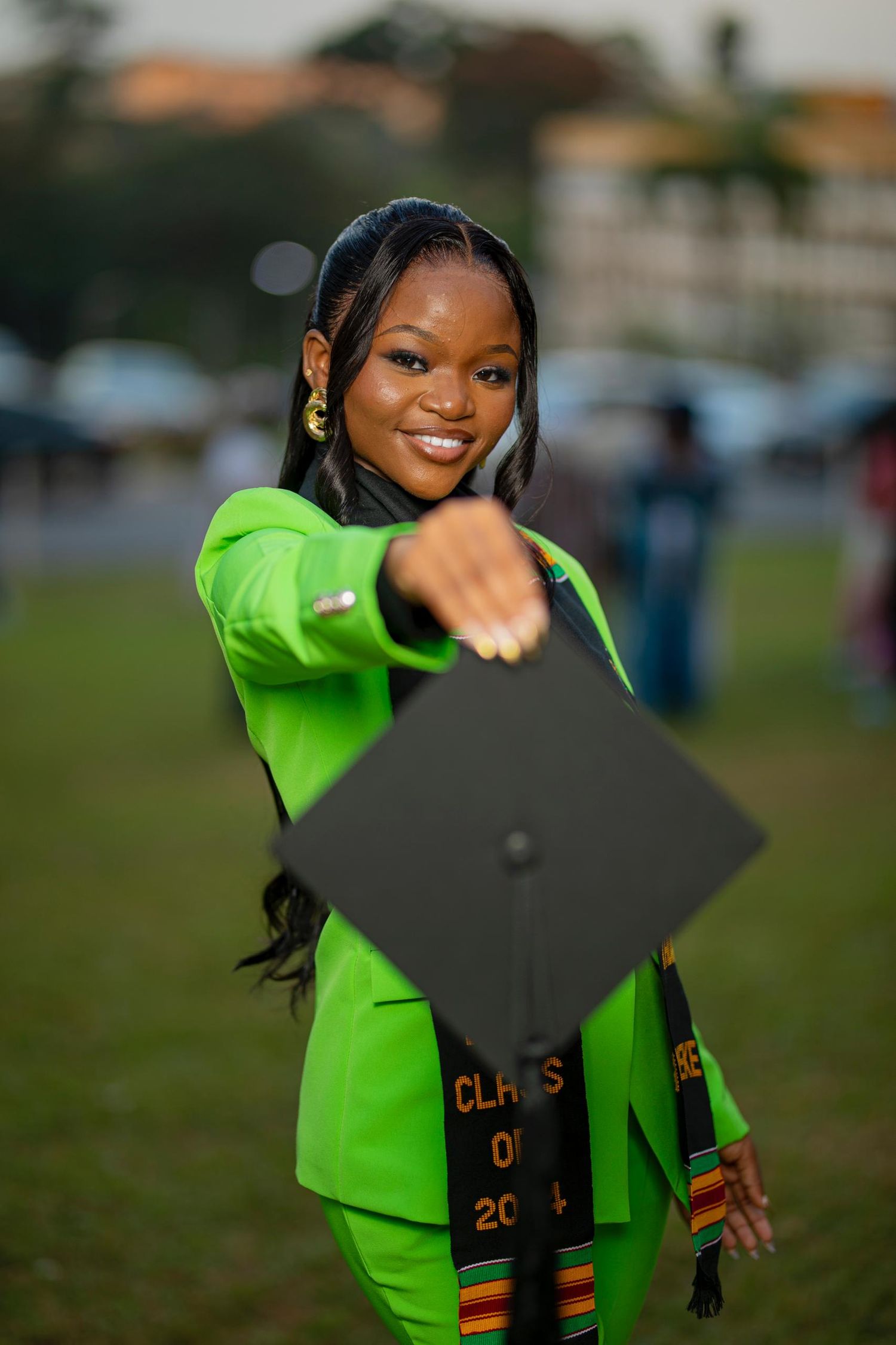 Graduate in bright lime green attire poses with graduation cap outdoors.