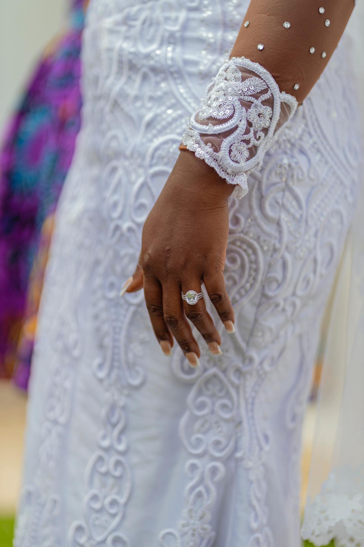 Close-up of delicate white lace bridal cuff and engagement ring on wedding dress.