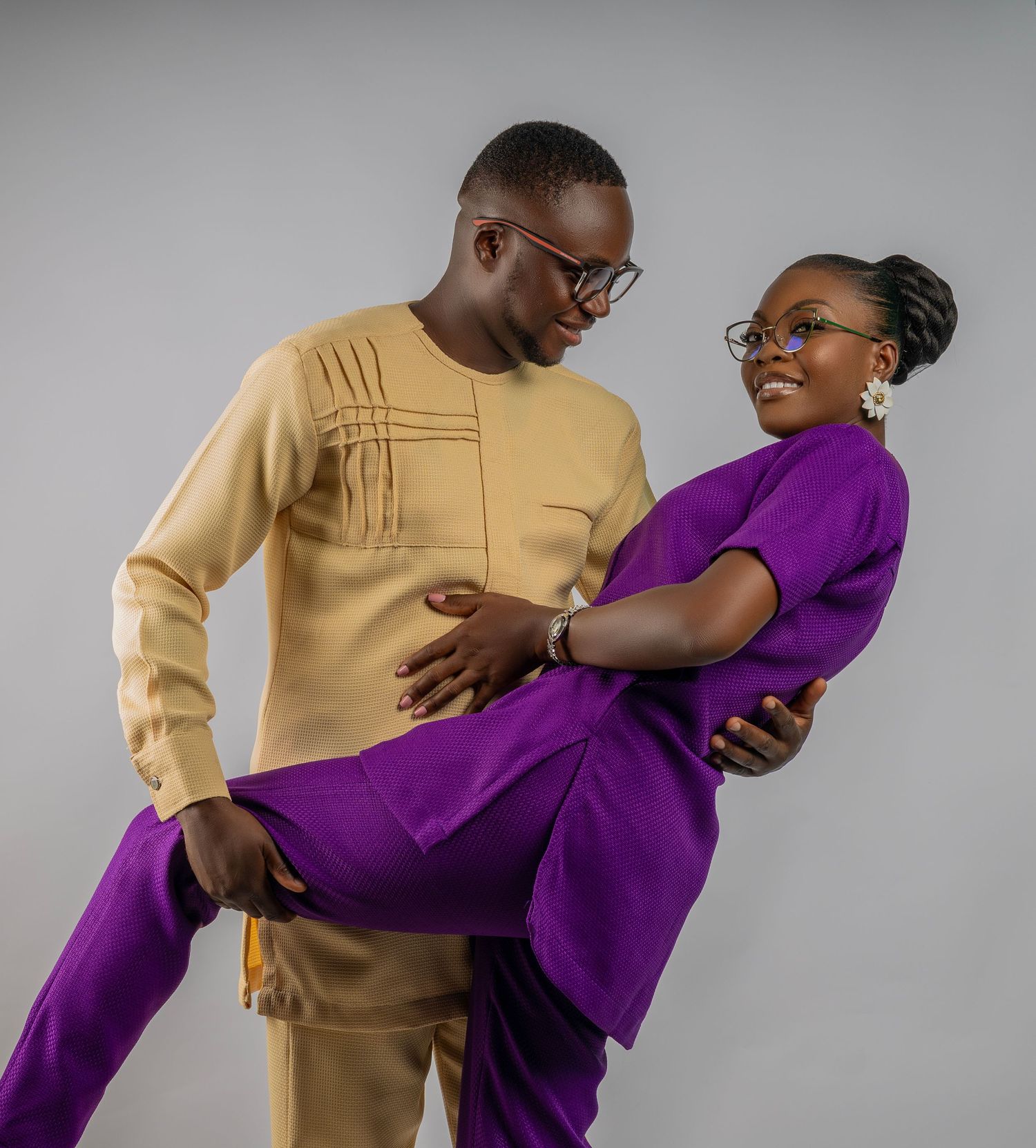 Two dancers perform an energetic duet in contrasting purple and beige outfits against a gray backdrop.