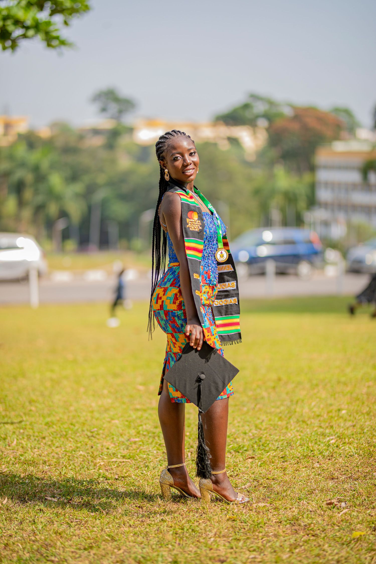 A child wearing a colorful African print backpack plays on a grassy field during a sunny day.