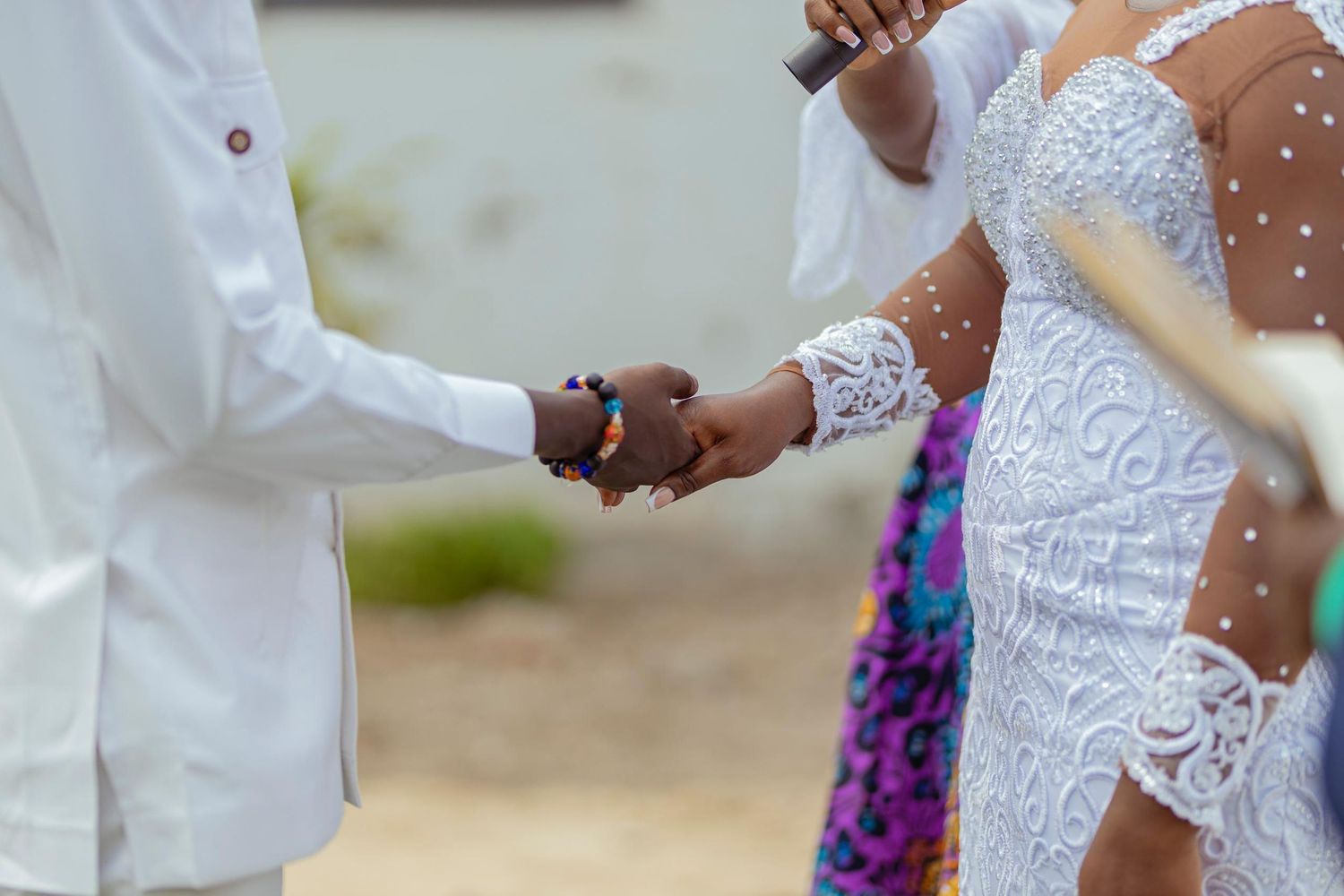 Close-up of hands exchanging rings during a wedding ceremony with intricate white lace details visible.