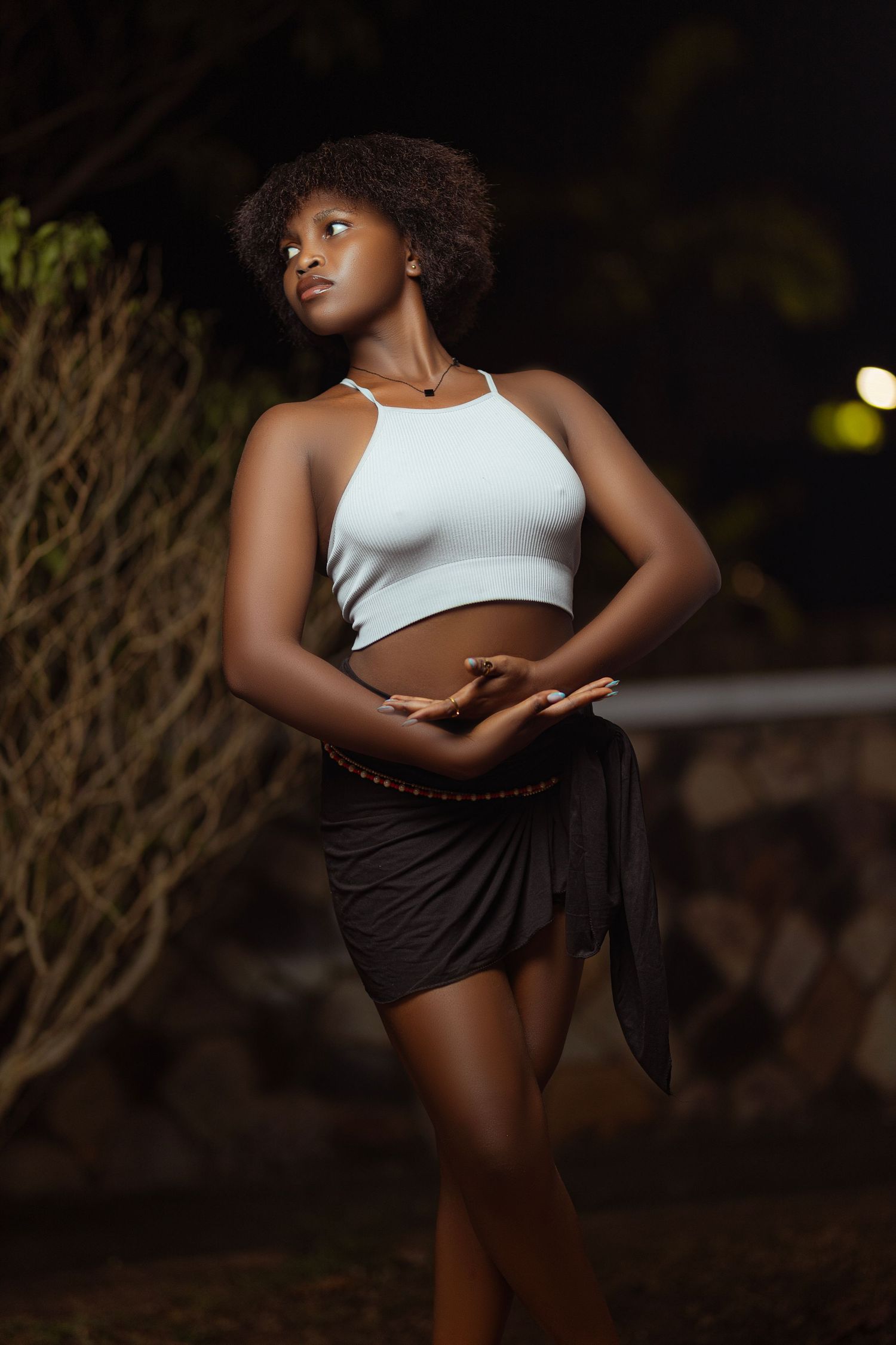 Artistic portrait of a model in white crop top and dark shorts against night backdrop.