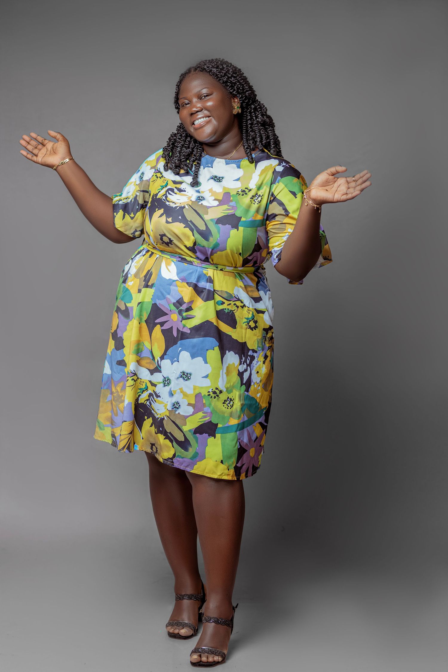Person in colorful floral print dress poses expressively against gray backdrop.