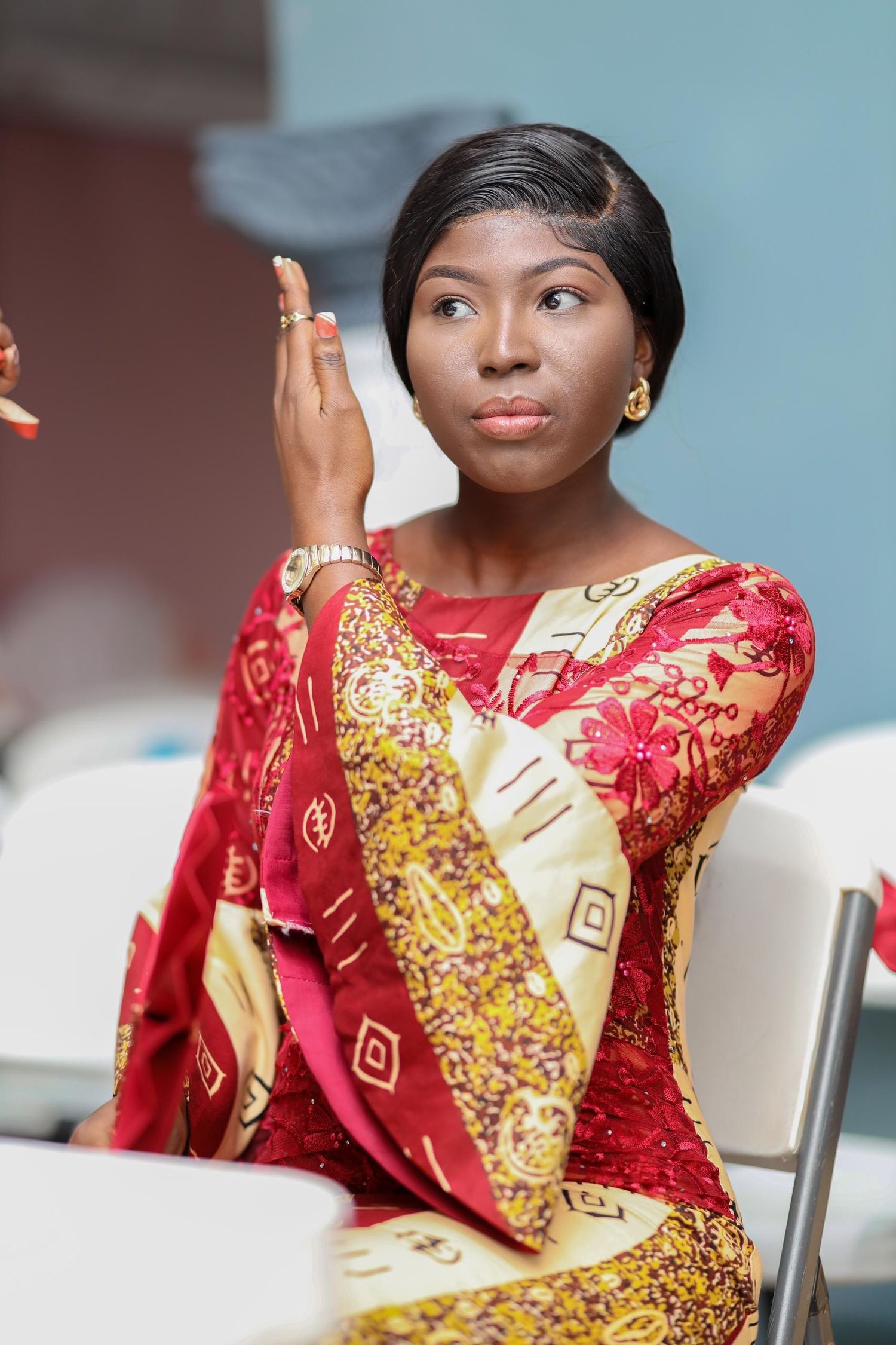 Woman in red and gold traditional dress gestures during conversation.