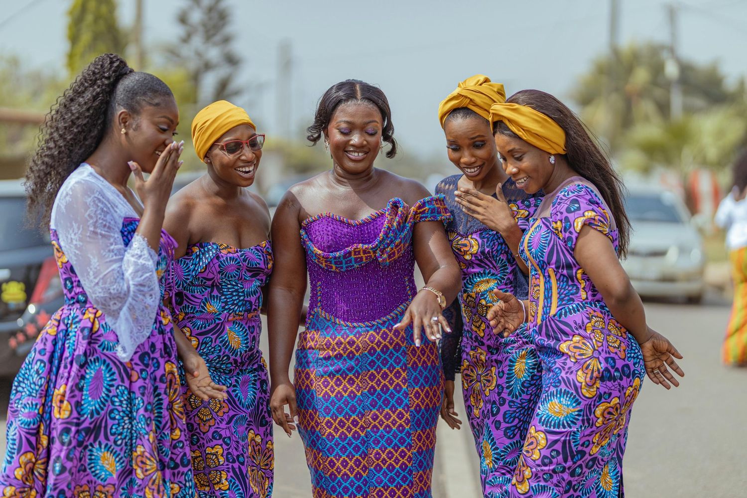 Group wearing colorful African print dresses and yellow headwraps share a joyful moment together.