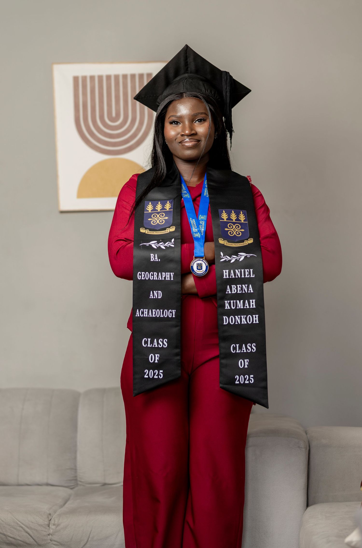 Graduate in red cap and gown wearing Class of 2025 stole for Geography and Archaeology degree poses proudly.
