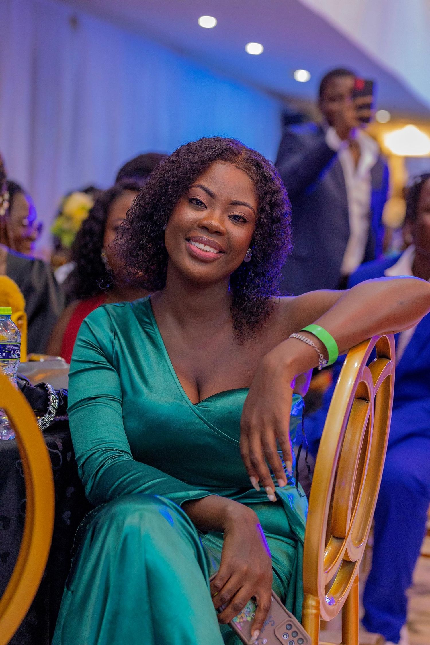 Elegant attendee in emerald green dress with curly hair enjoying a formal event.