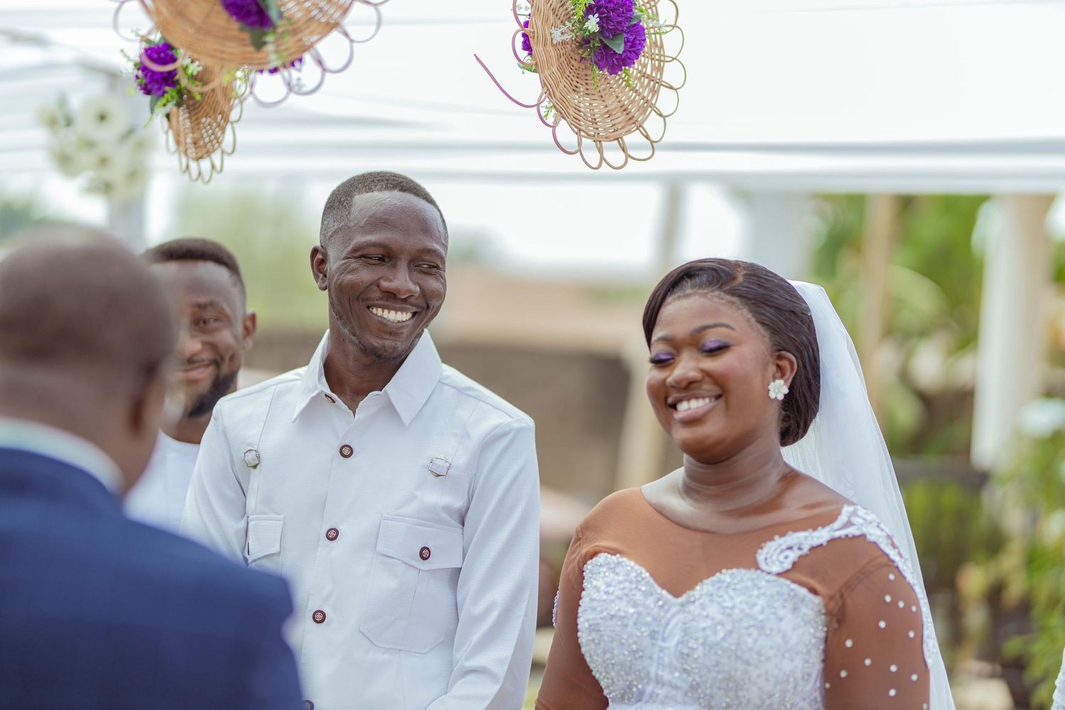 A couple shares joyful laughter during their wedding ceremony under decorative floral arrangements.