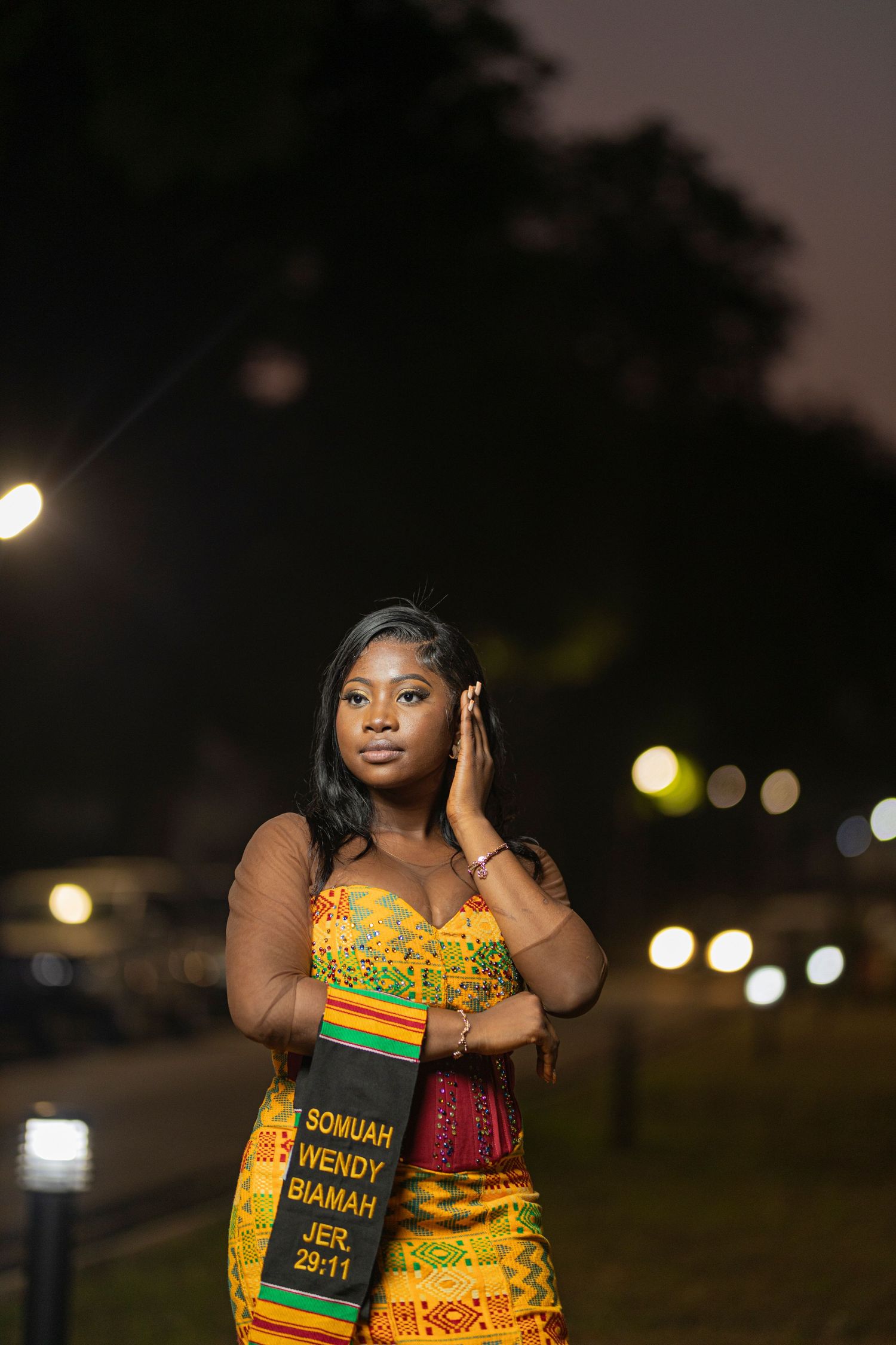 Person in yellow and red traditional dress poses at night with bokeh lighting.