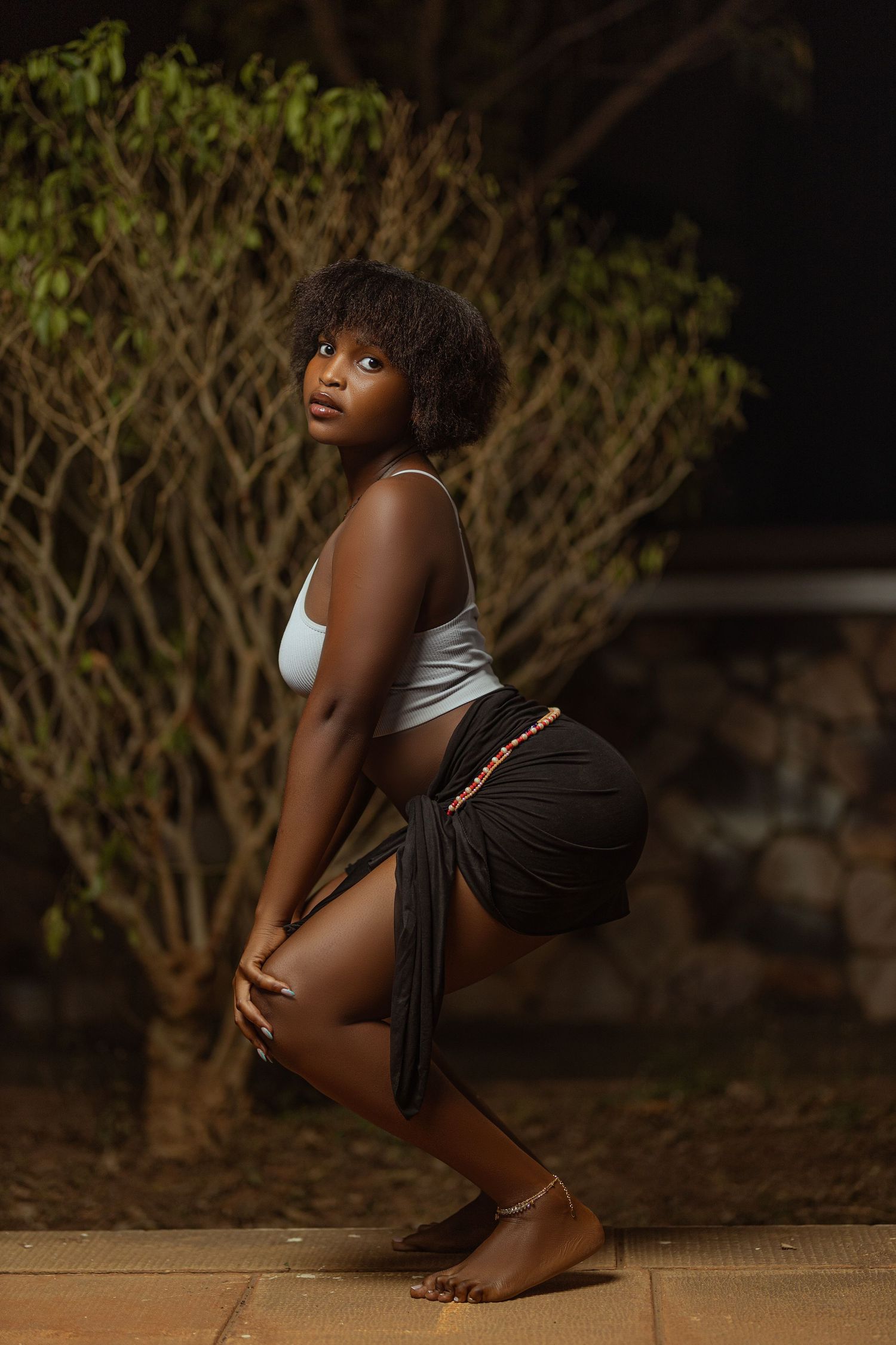 Person in white tank top and dark shorts poses artistically at night.