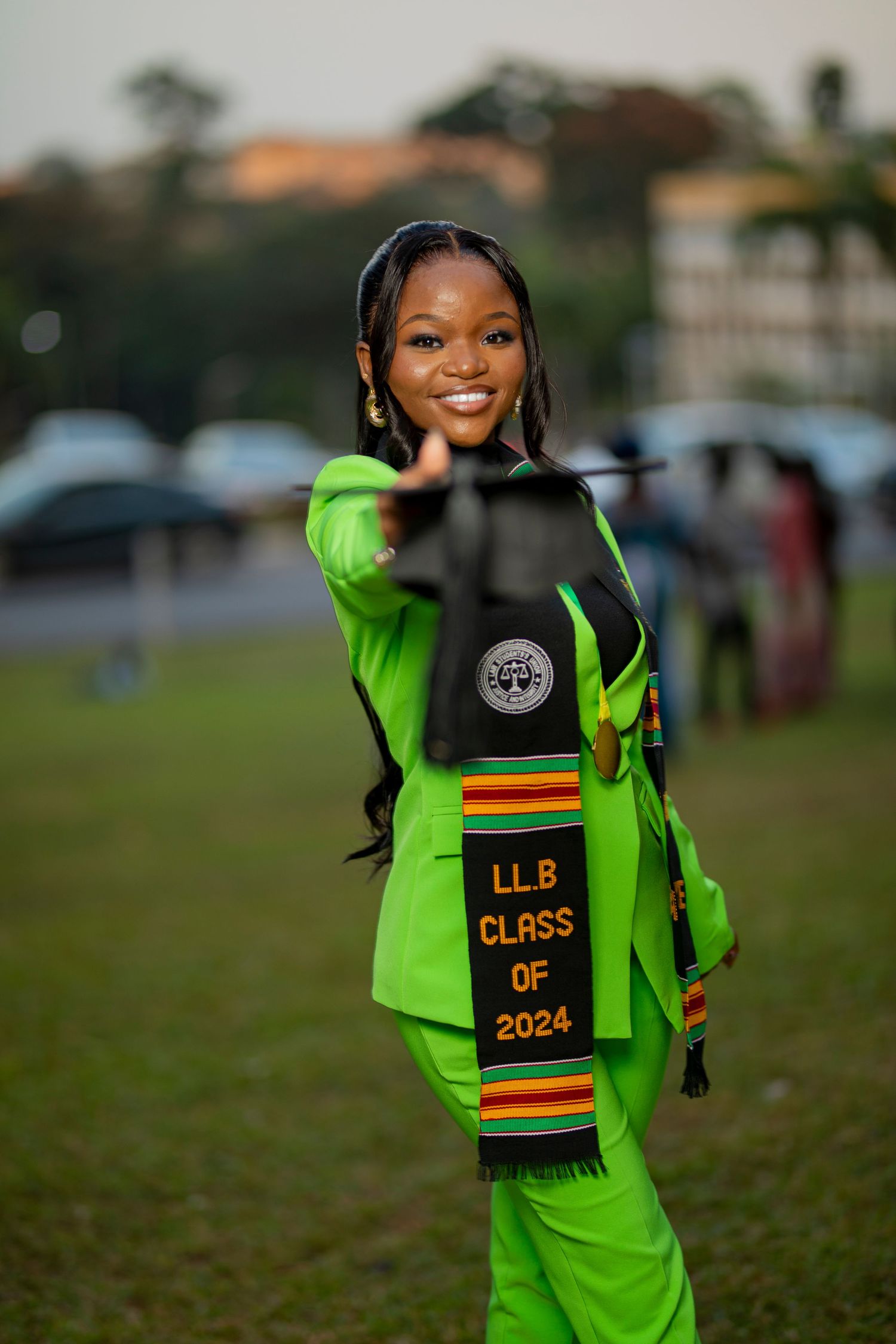 Graduate in bright neon green graduation attire poses outdoors with a decorative black and orange sash.