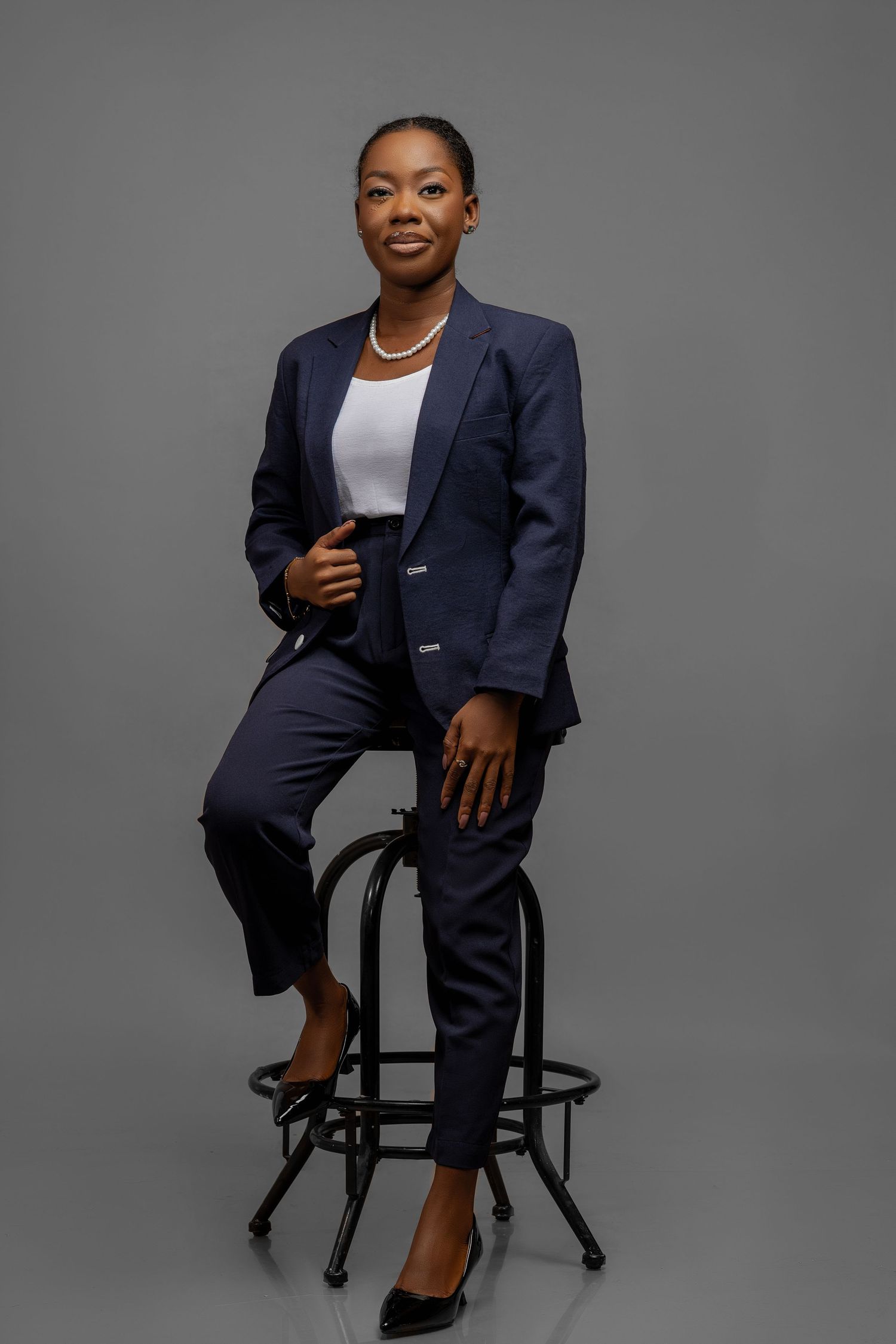 Professional studio portrait of someone in a navy suit jacket seated on an office chair against a gray backdrop.