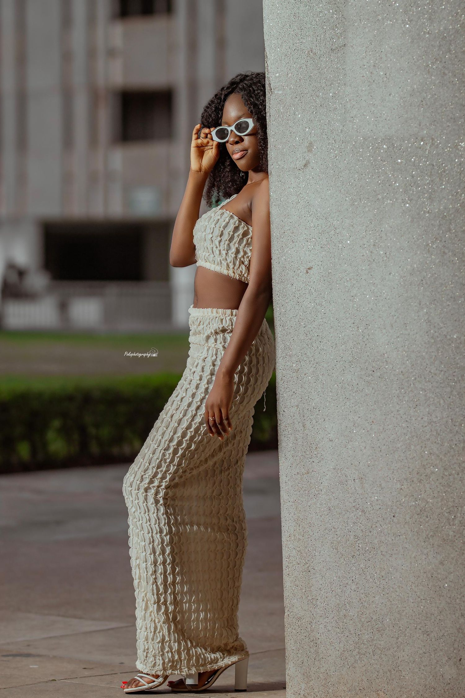 Fashionable cream knit two-piece outfit paired with glasses in architectural setting.