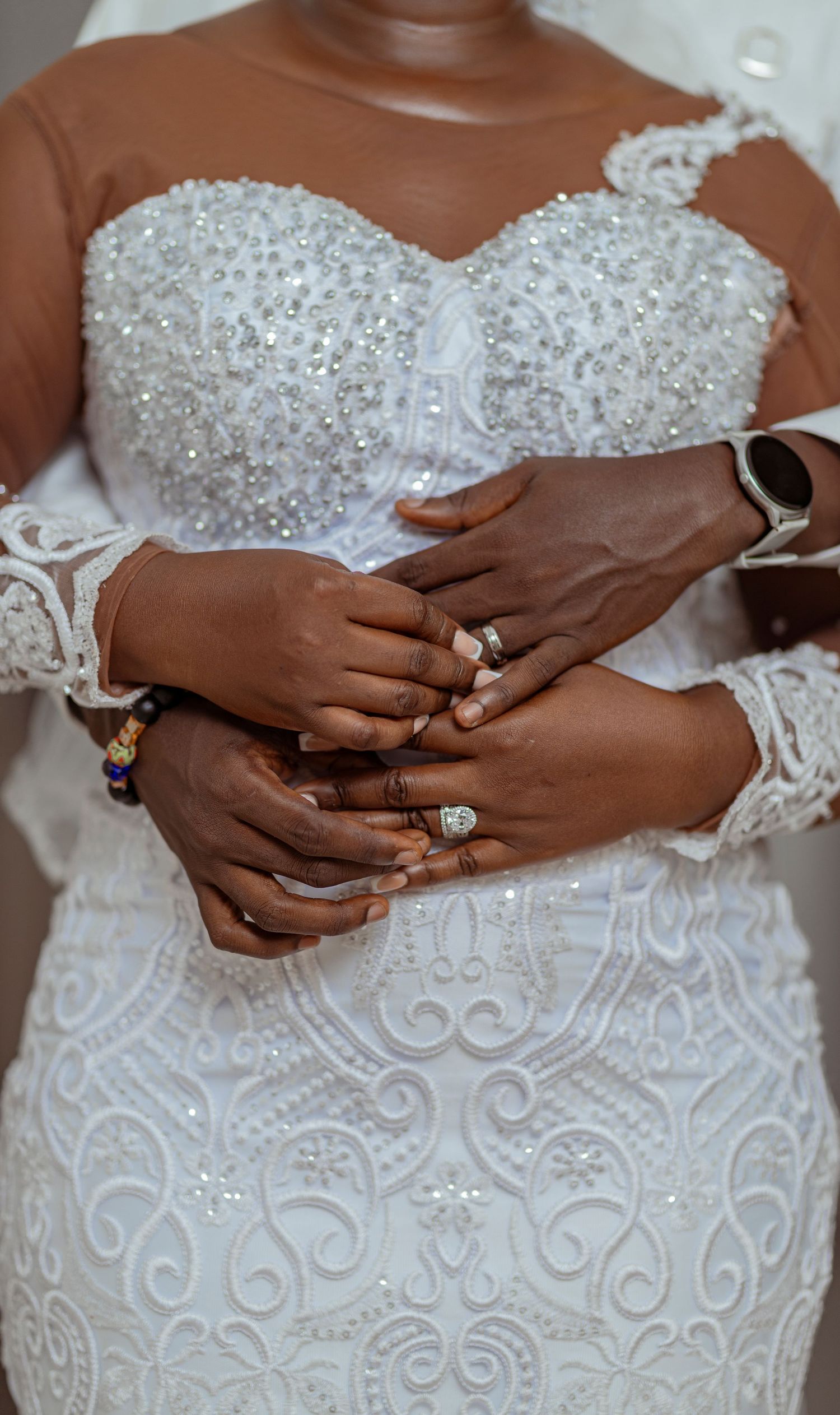Close-up of hands showing off wedding rings on an ornate white lace dress.