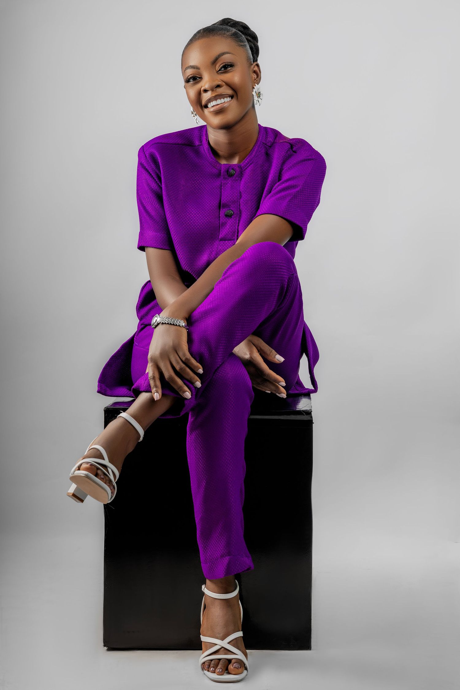 A series of photos showing someone in a vibrant purple outfit sitting on a black cube against a light gray backdrop.