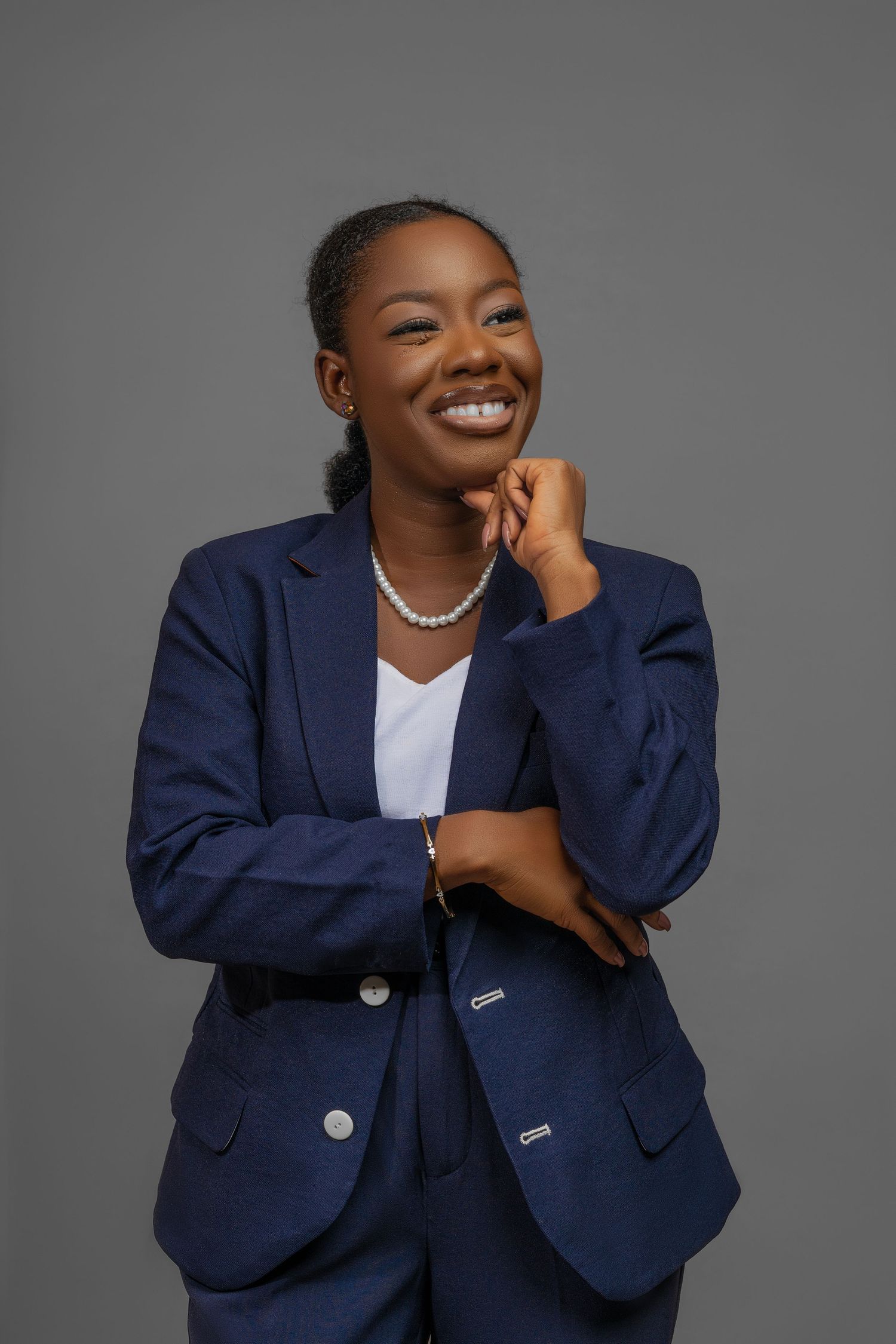 A person in a navy blue blazer and white top laughs expressively against a gray studio backdrop.