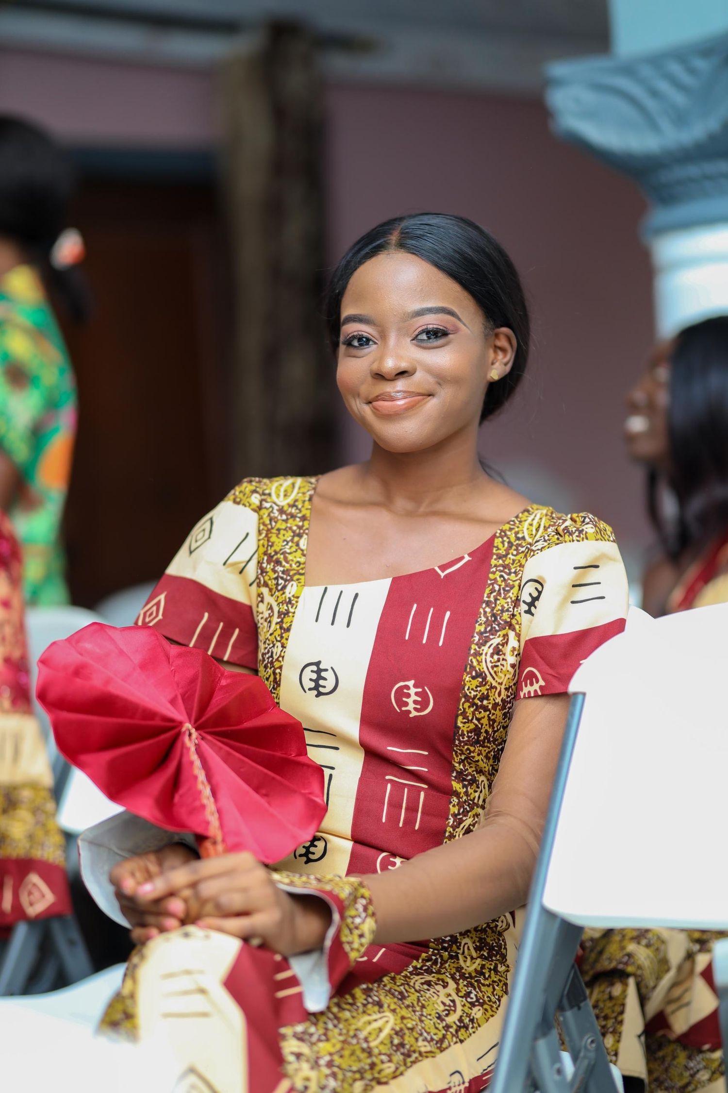 Traditional African wedding guest in colorful attire holding a decorative red bow.