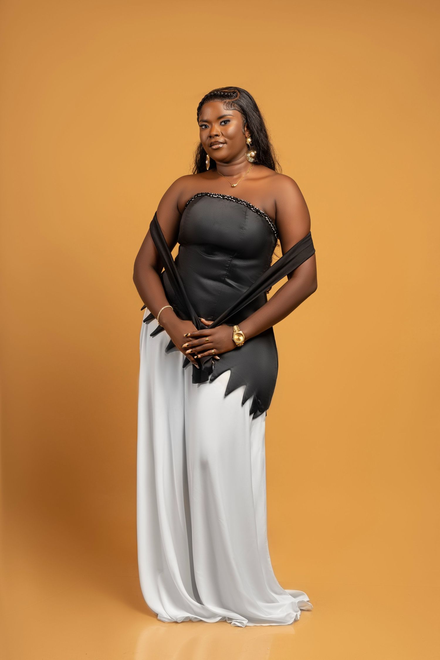 Woman in black and white dress poses gracefully against orange background in fashion photoshoot series.