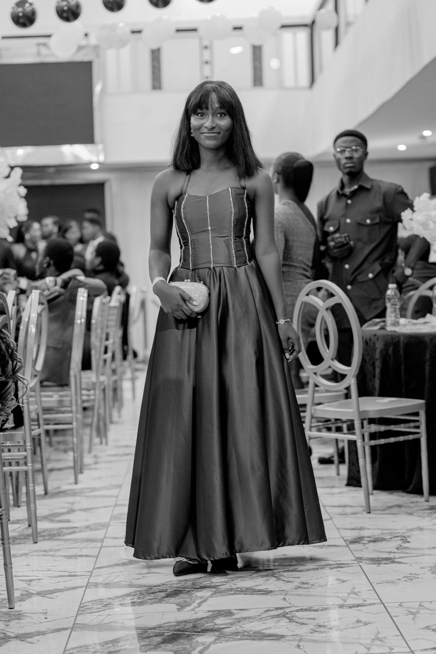 Black and white photo of woman in elegant full-length gown at formal event venue.
