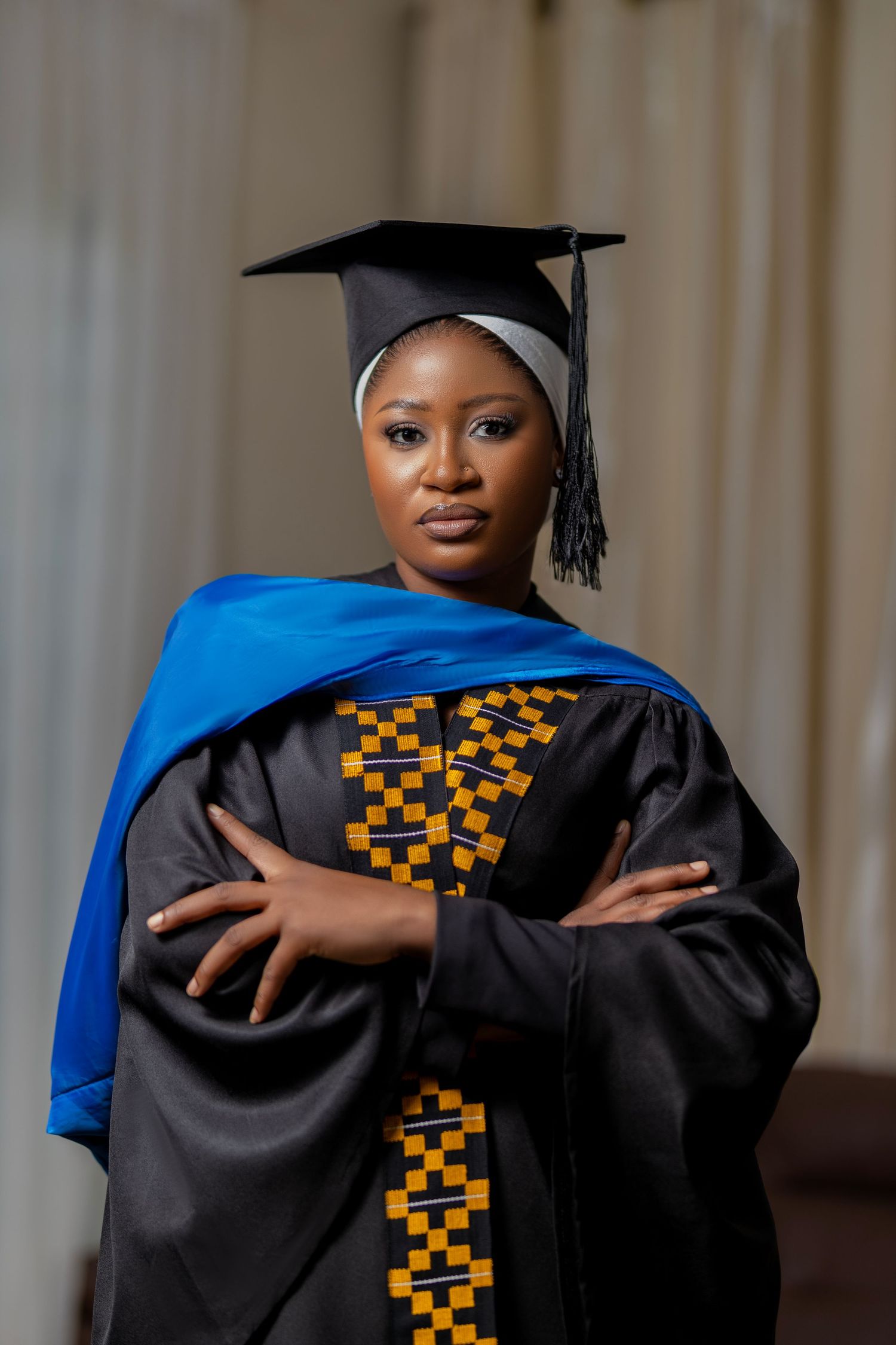 Graduate wearing traditional black academic regalia with blue stole and gold kente cloth pattern stands confidently.