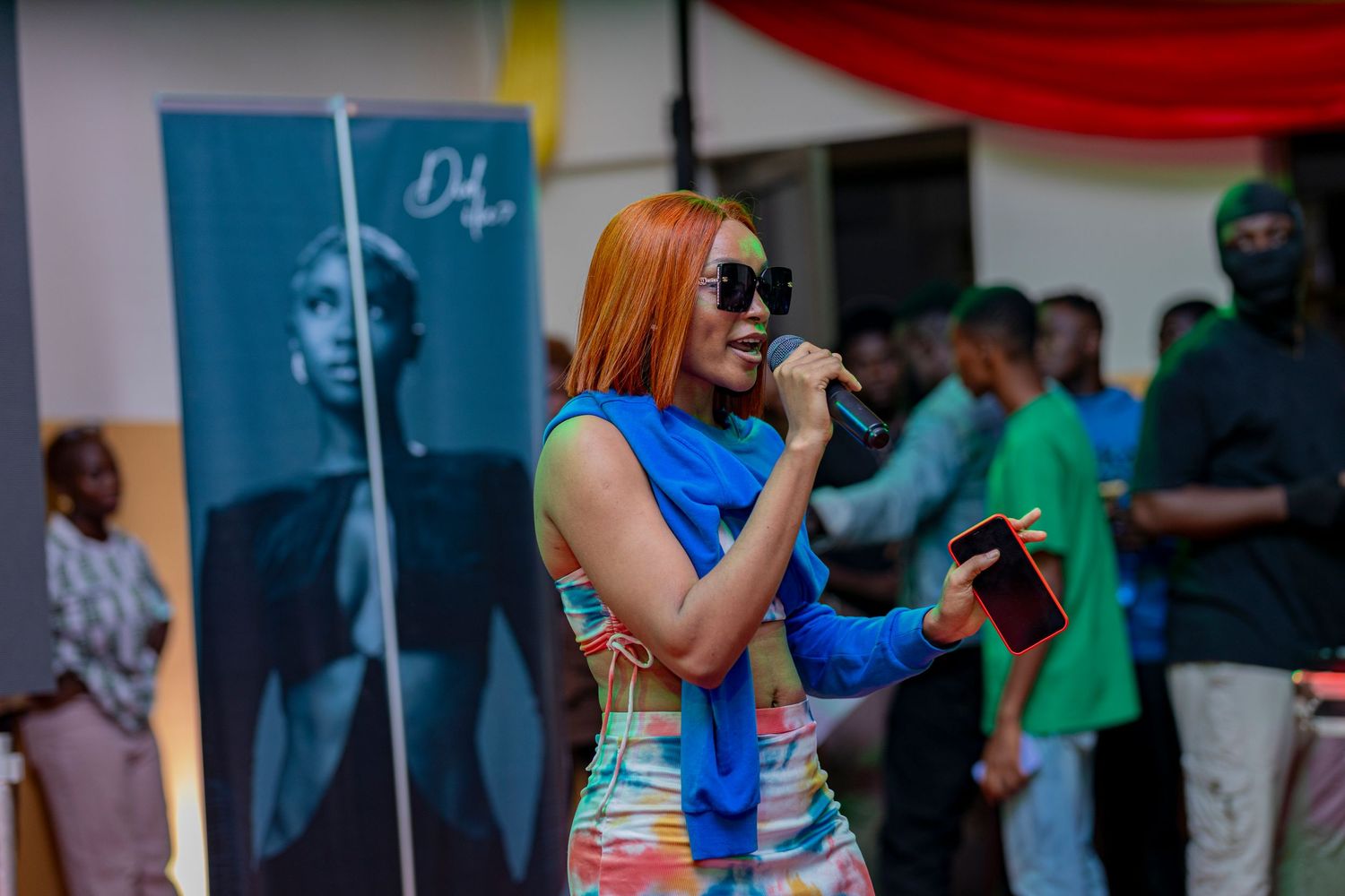 Artist with orange hair performs in blue top at outdoor music event.