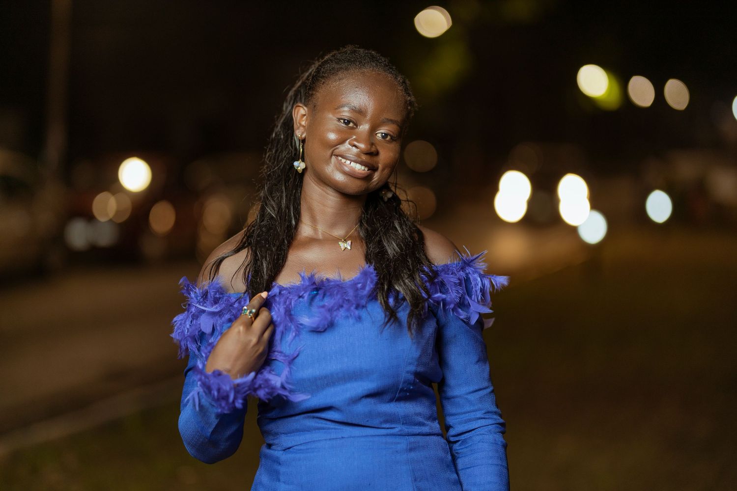 A person wearing a blue off-shoulder dress smiles under night lighting.