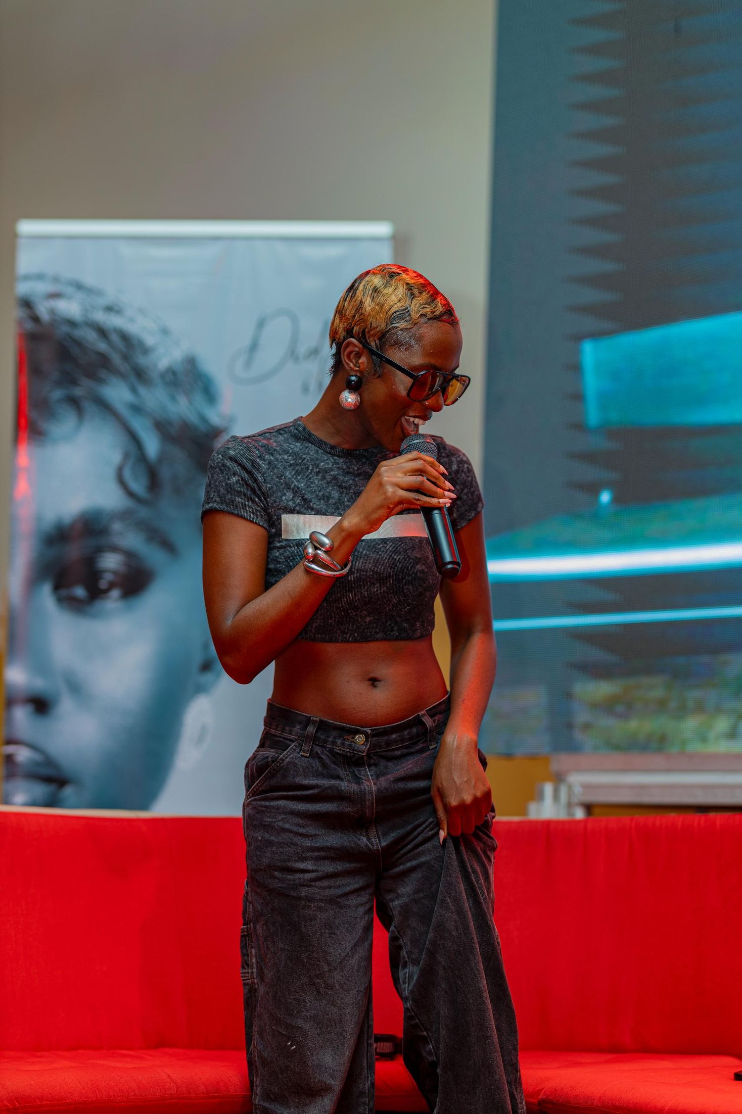 Artist performing on stage with red couch and artistic backdrop.