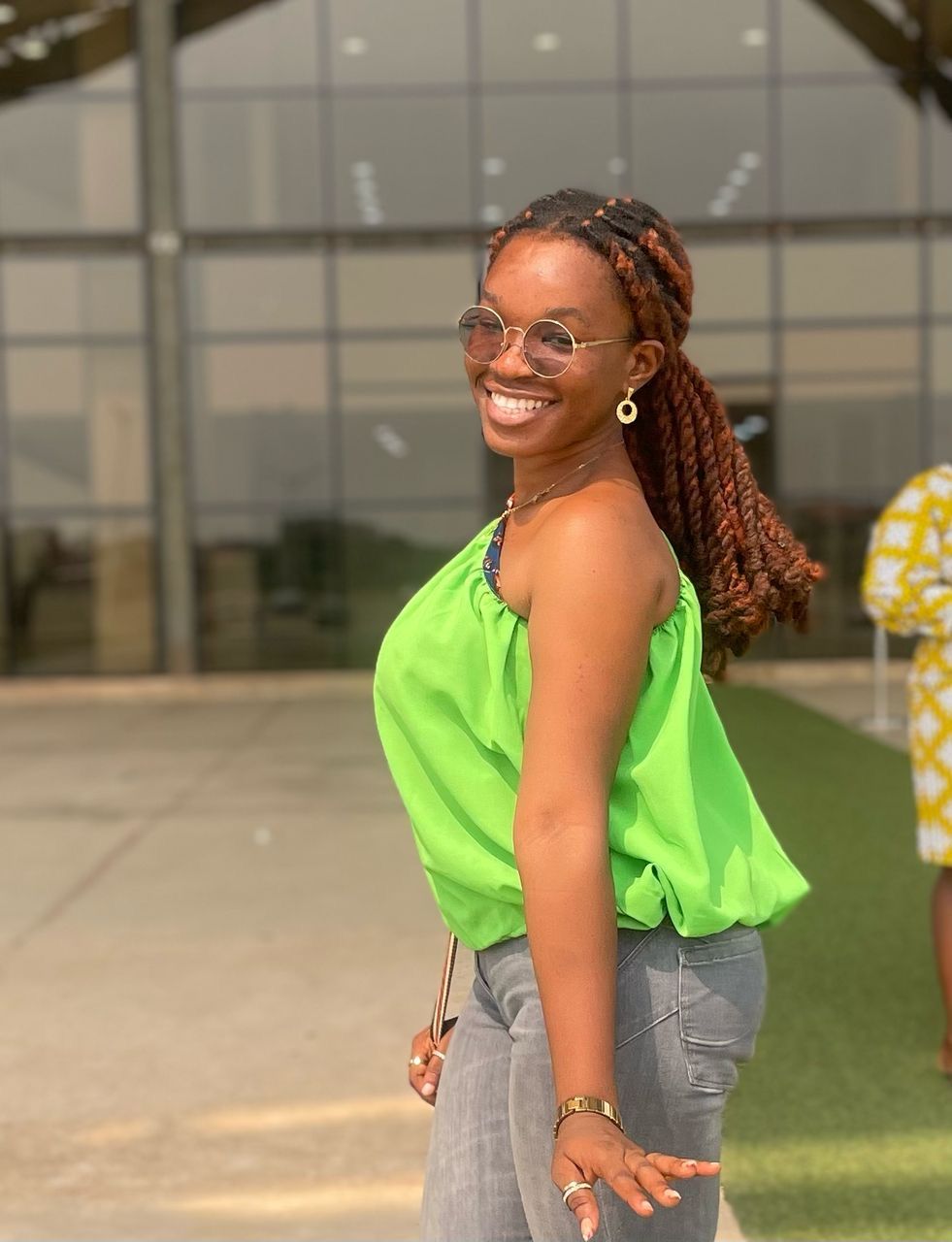 A person in a bright green top and jeans poses confidently outside a modern building.