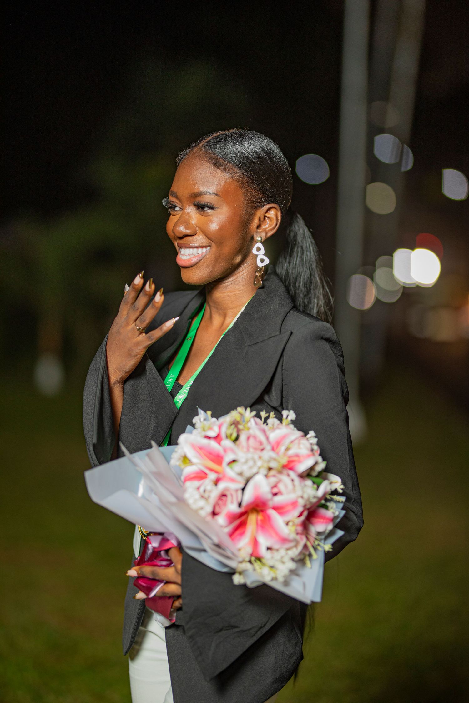 A joyful smile lights up the evening as someone holds a beautiful bouquet of pink lilies while wearing a black blazer.