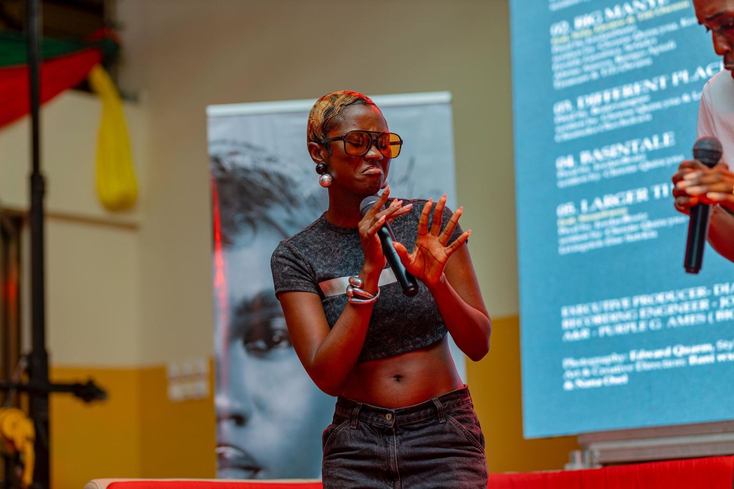 Stage performer in crop top and jeans holds microphone during energetic show.