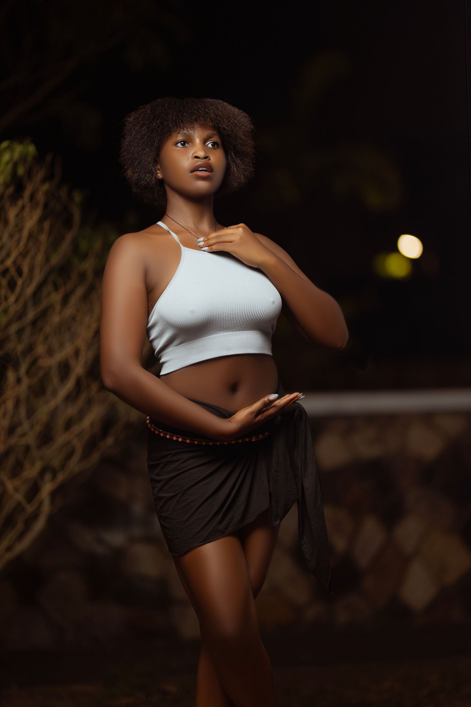 Person in white crop top poses dramatically against dark background.