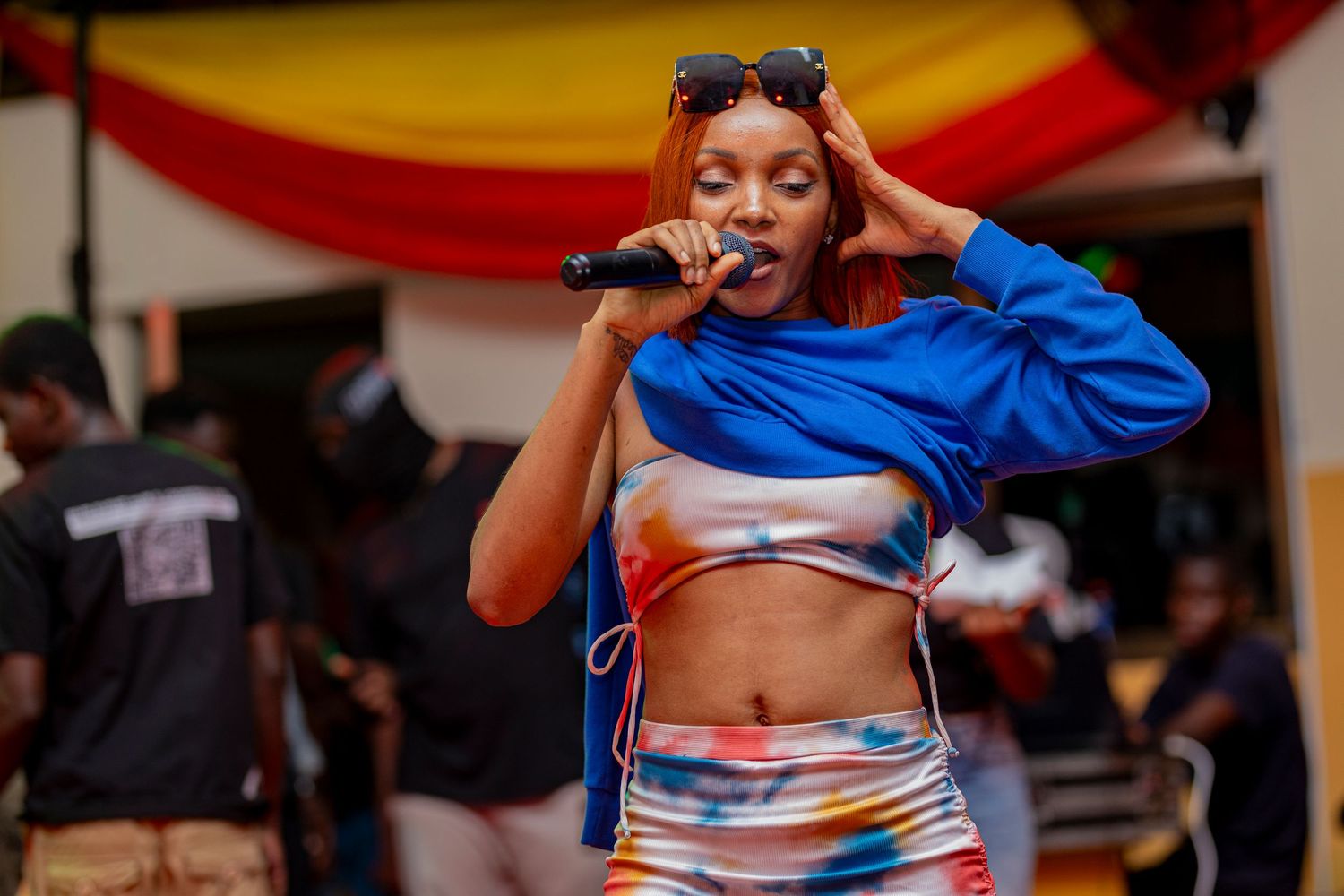 Singer in blue outfit performs energetically at outdoor event with red and yellow decor.